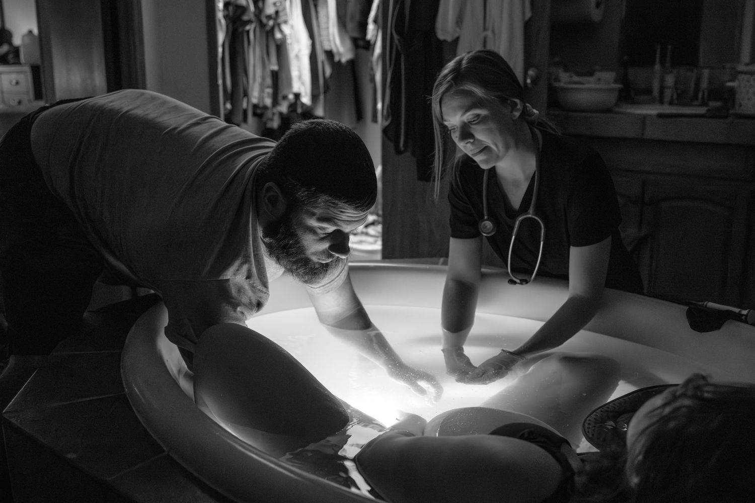 Medical professionals conducting examination under bright focused lighting. Wichita birth photographer documenting a home birth