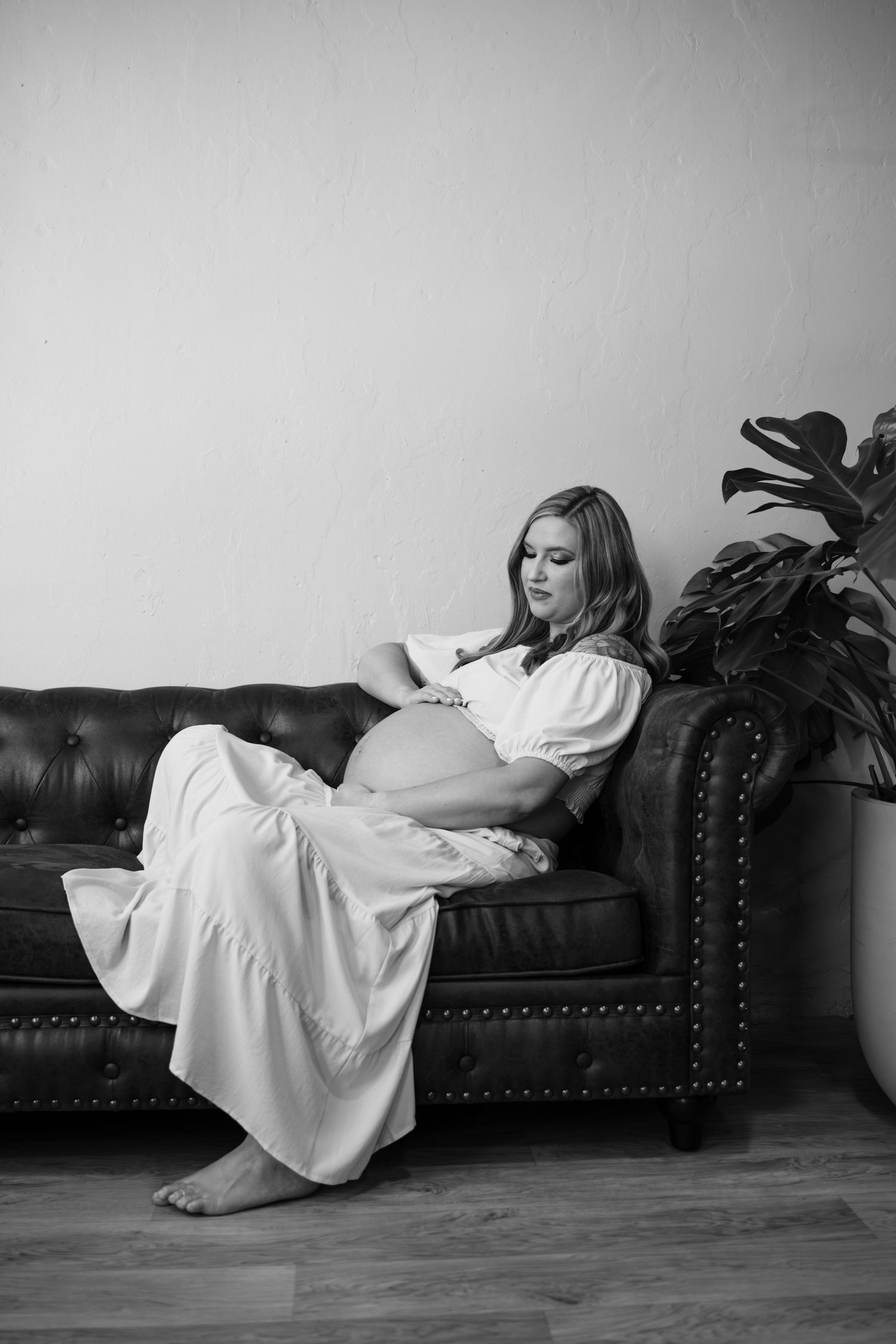 Artistic black and white photos of woman in white dress posing on leather couch. Wichita, Kansas Maternity Photography