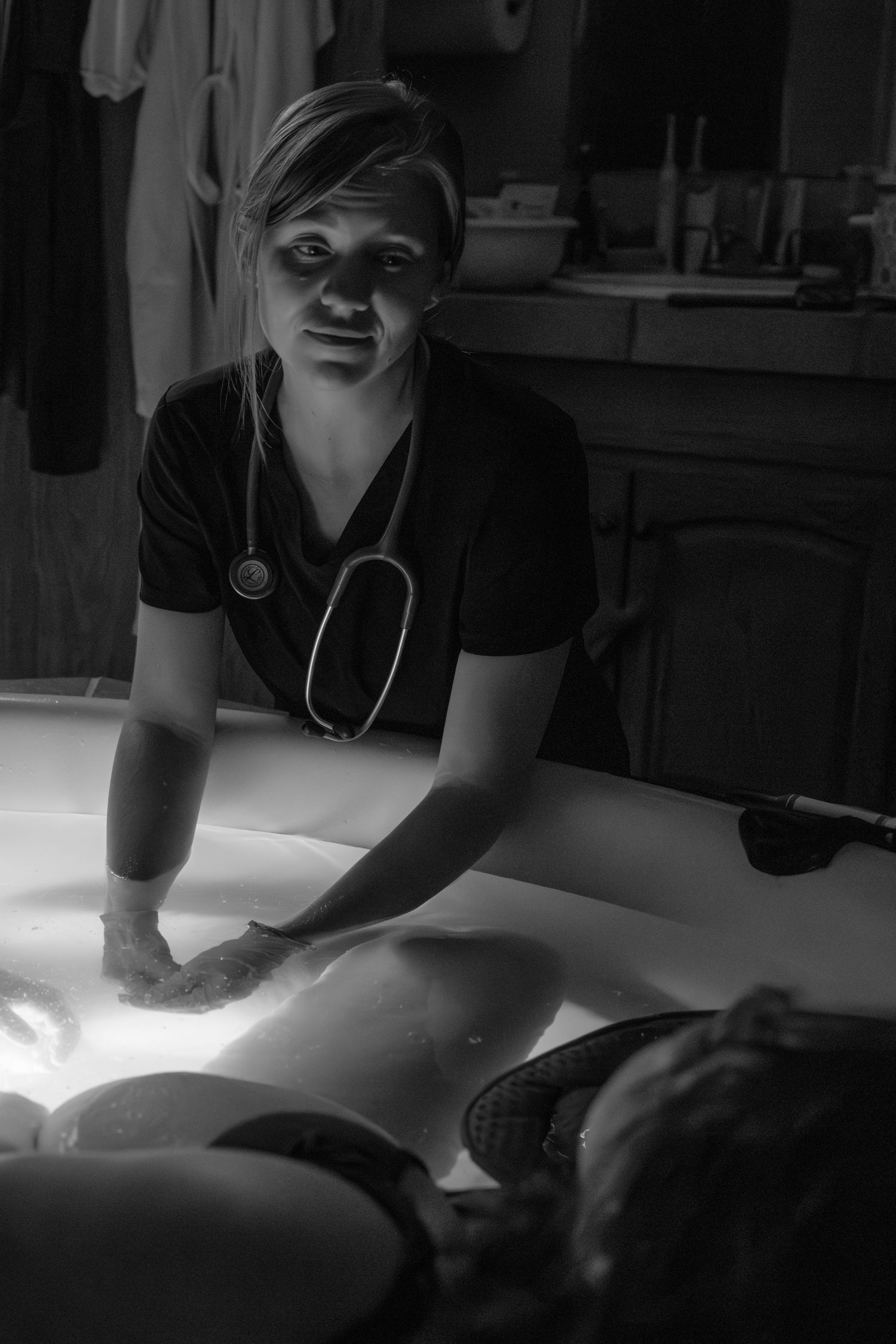 Healthcare worker with stethoscope performing medical examination in dramatic lighting. Wichita birth photographer documenting a home birth