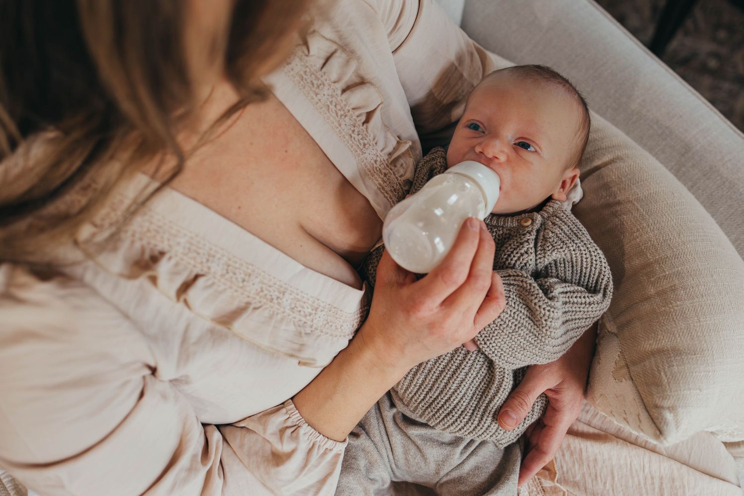 Newborn baby wrapped in a soft knitted blanket being gently held by caring hands.
