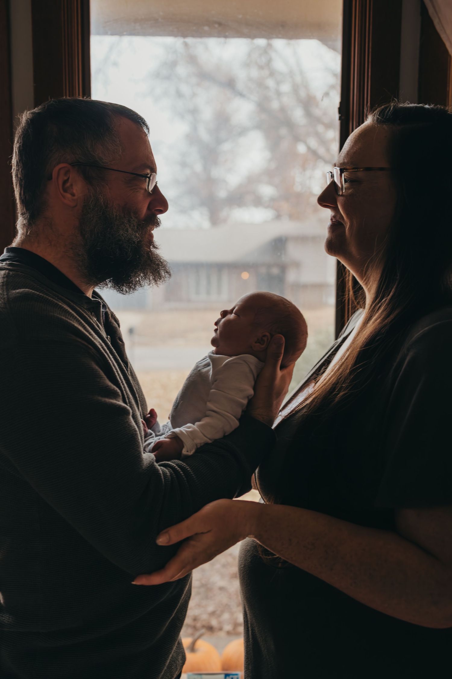 A silhouetted family shares tender moments together near a window in moody lighting.
