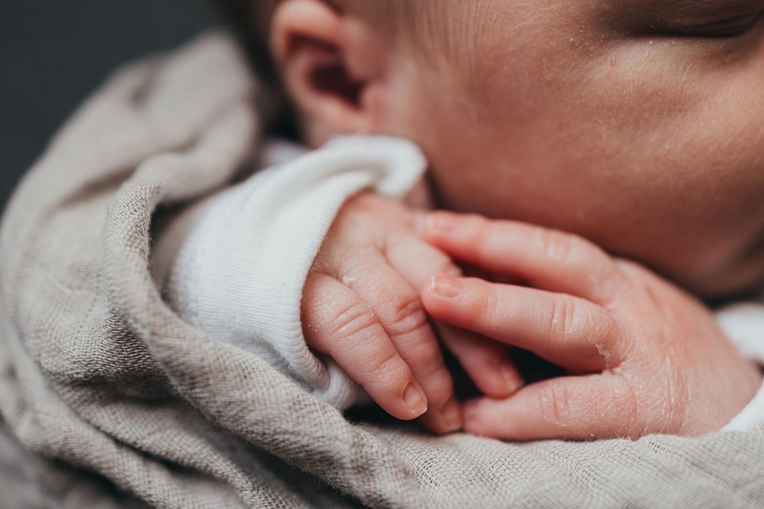 Close-up photo of a tiny baby hand resting on soft gray blanket showing delicate newborn details.
