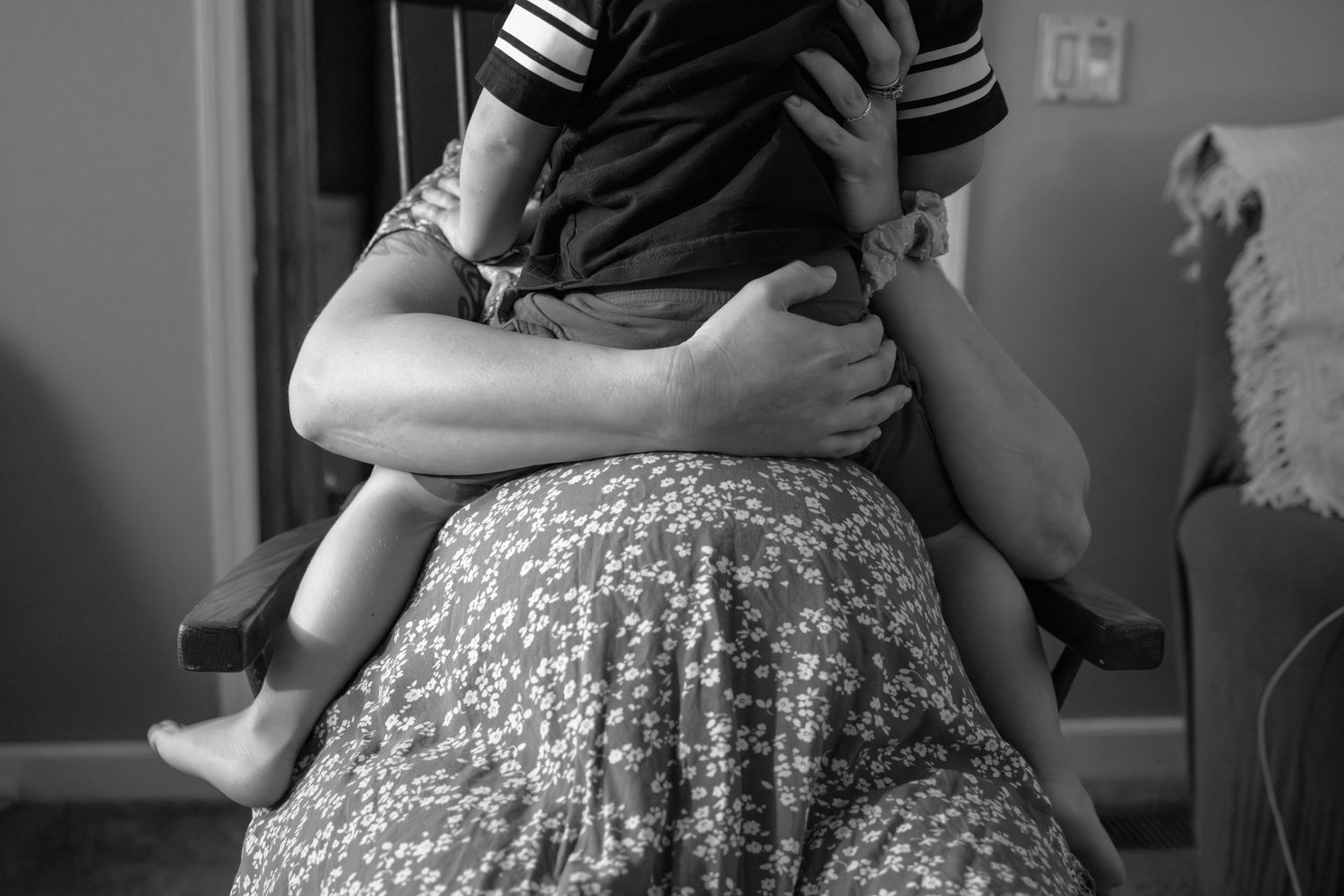 Black and white image of a child sitting on someone wearing a patterned dress.