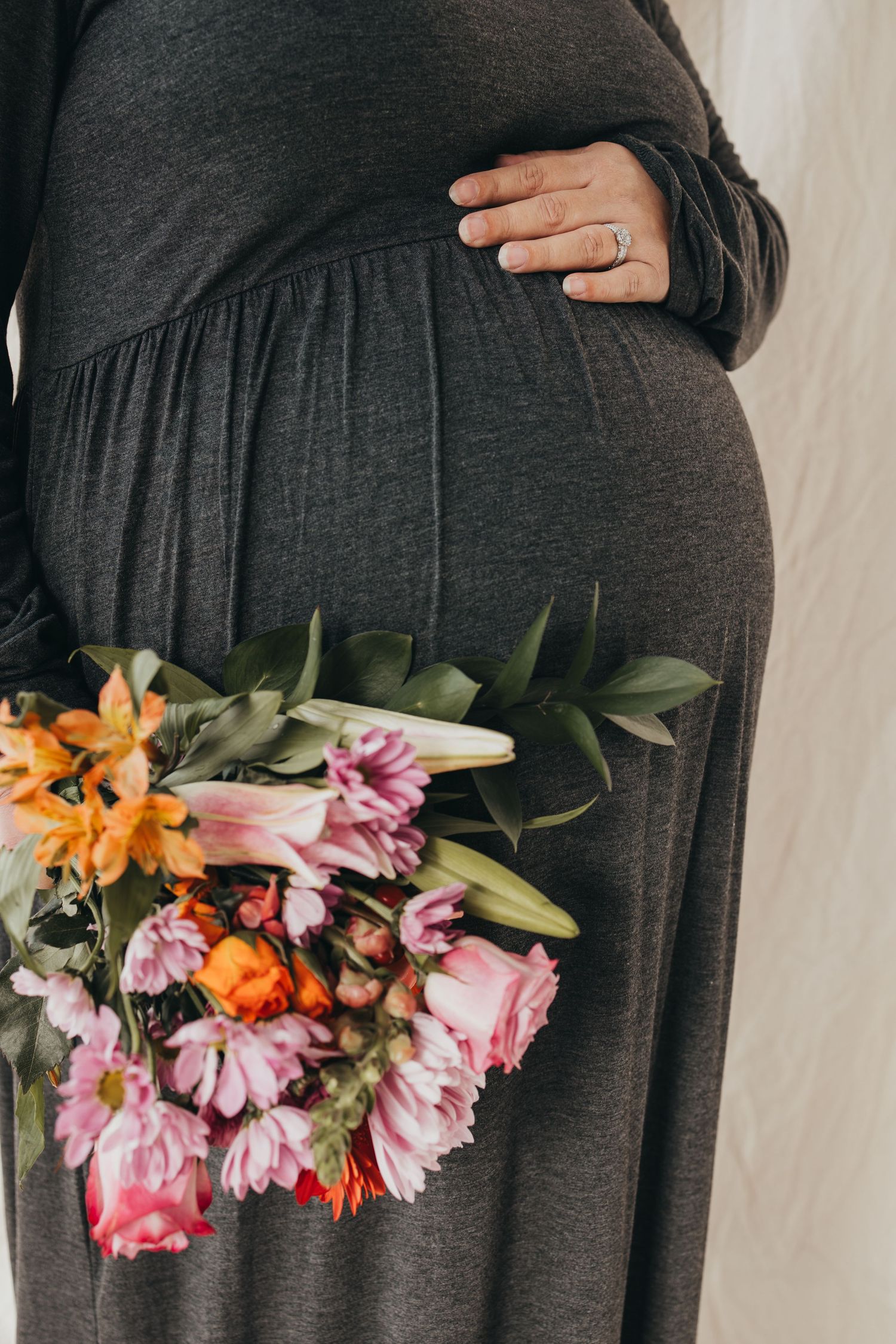 Close-up of baby bump with vibrant pink and orange flowers laid across.