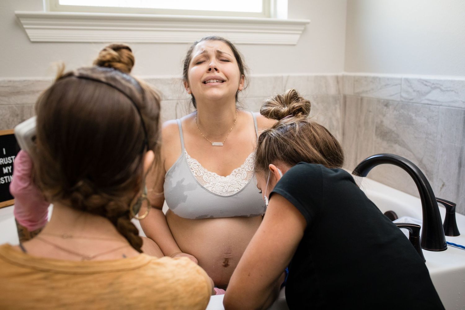 Support person assists laboring woman in bathtub during birth.