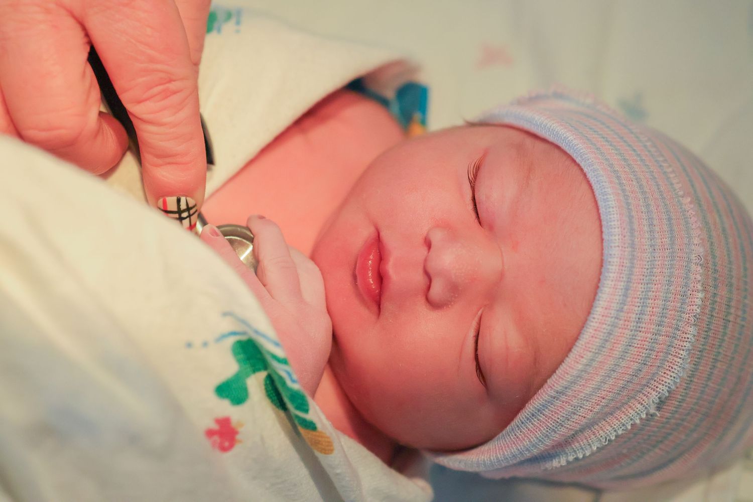 Peaceful newborn baby wearing striped hospital cap resting after birth.