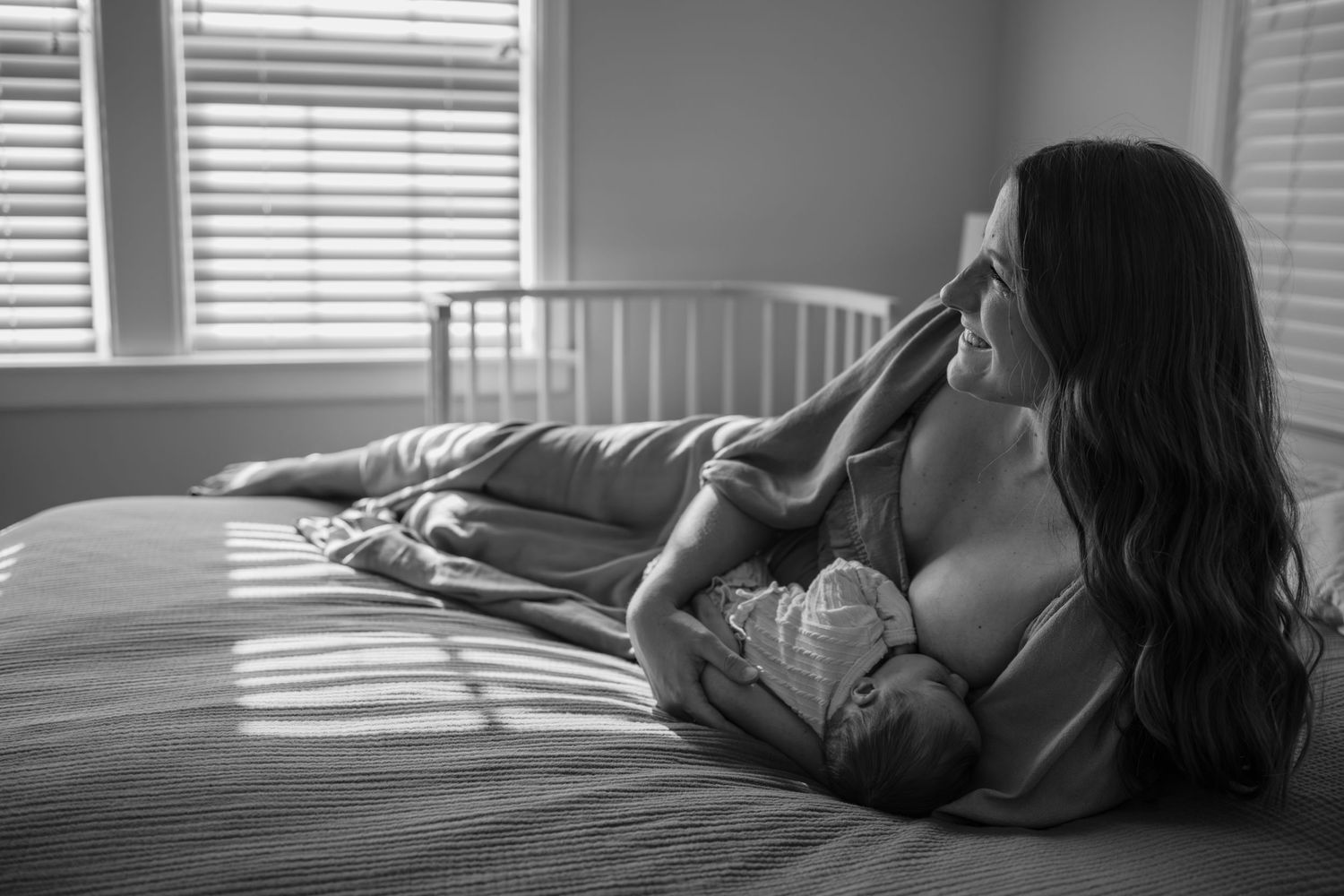 Person resting on bed with sunlight streaming through window blinds.