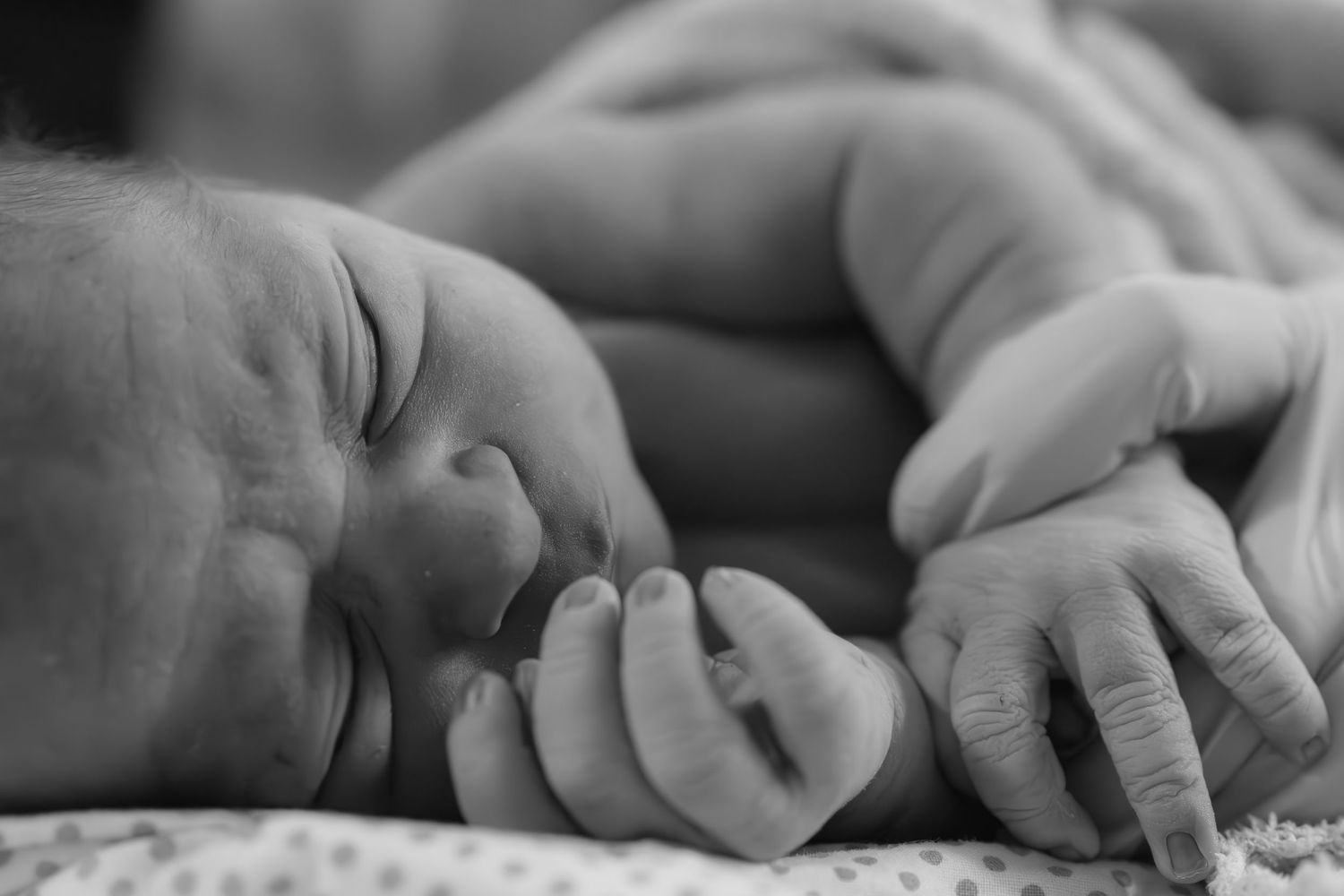 Close-up of hands recording baby footprints on a white surface.