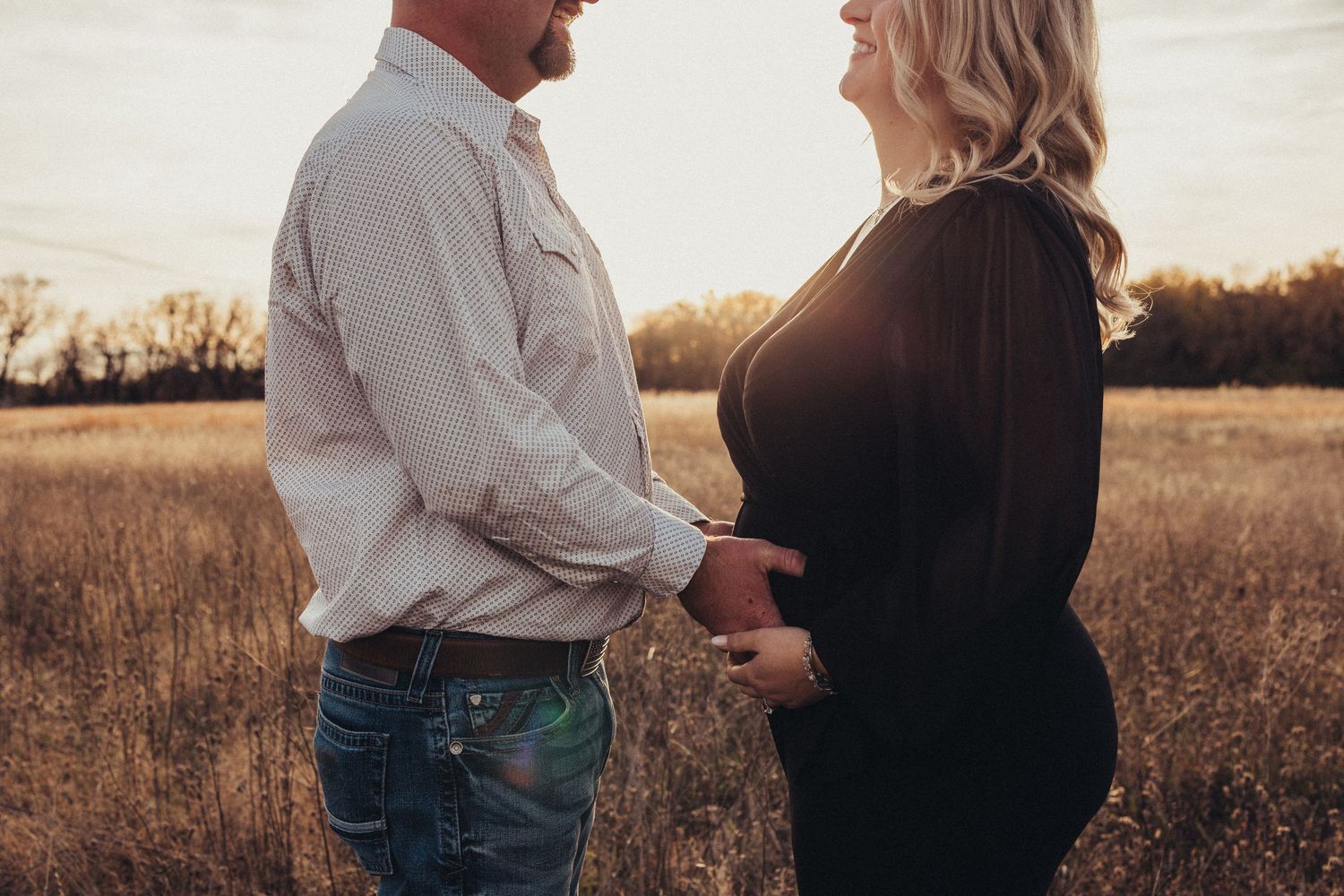 Expecting couple shares intimate moment in golden field at dusk.