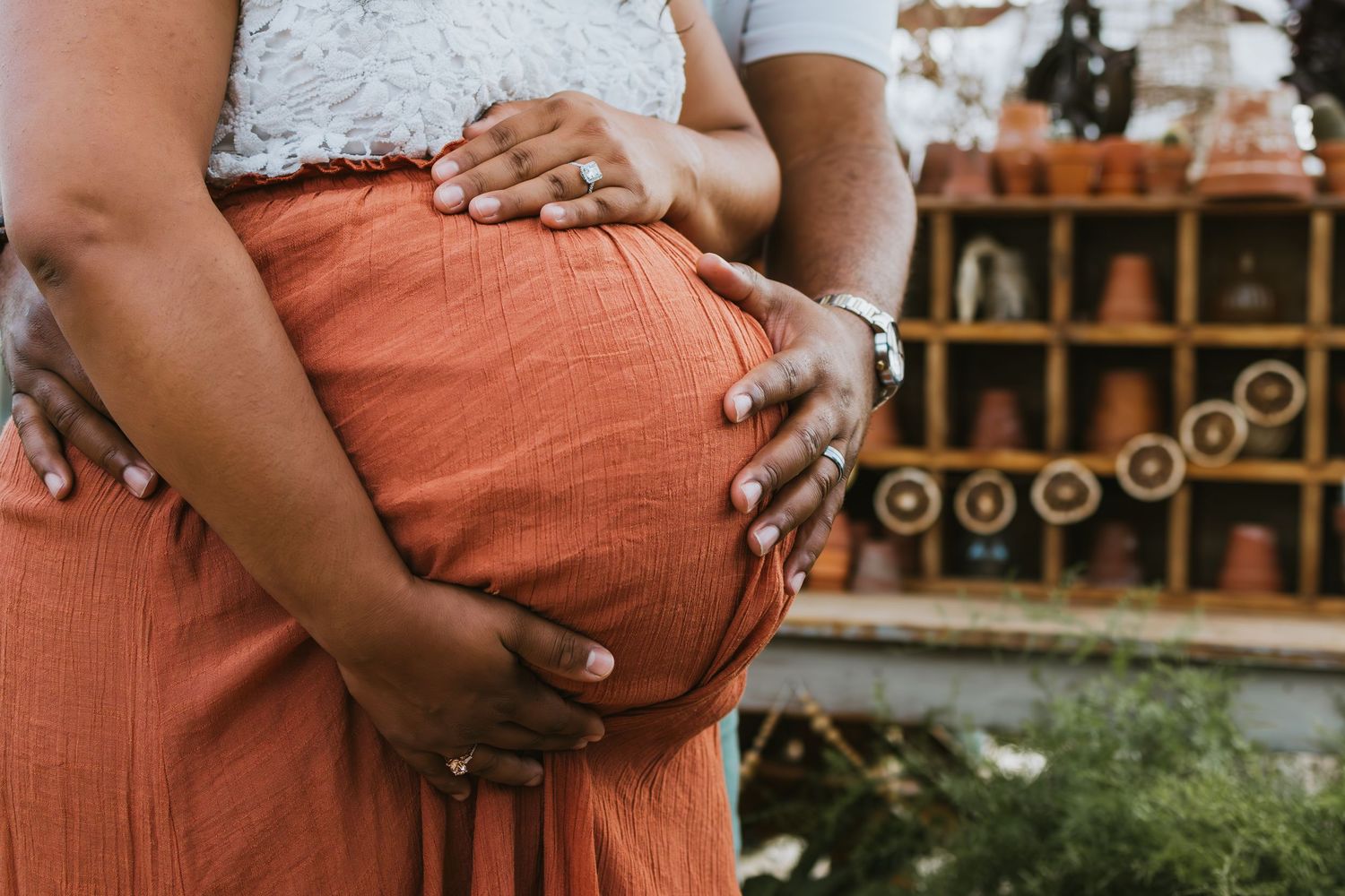 A maternity photoshoot in a field with orange dress and white flowers in golden sunlight.