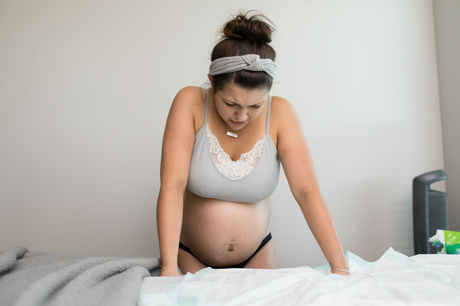 Woman in gray top resting on bed during labor or birth preparation.