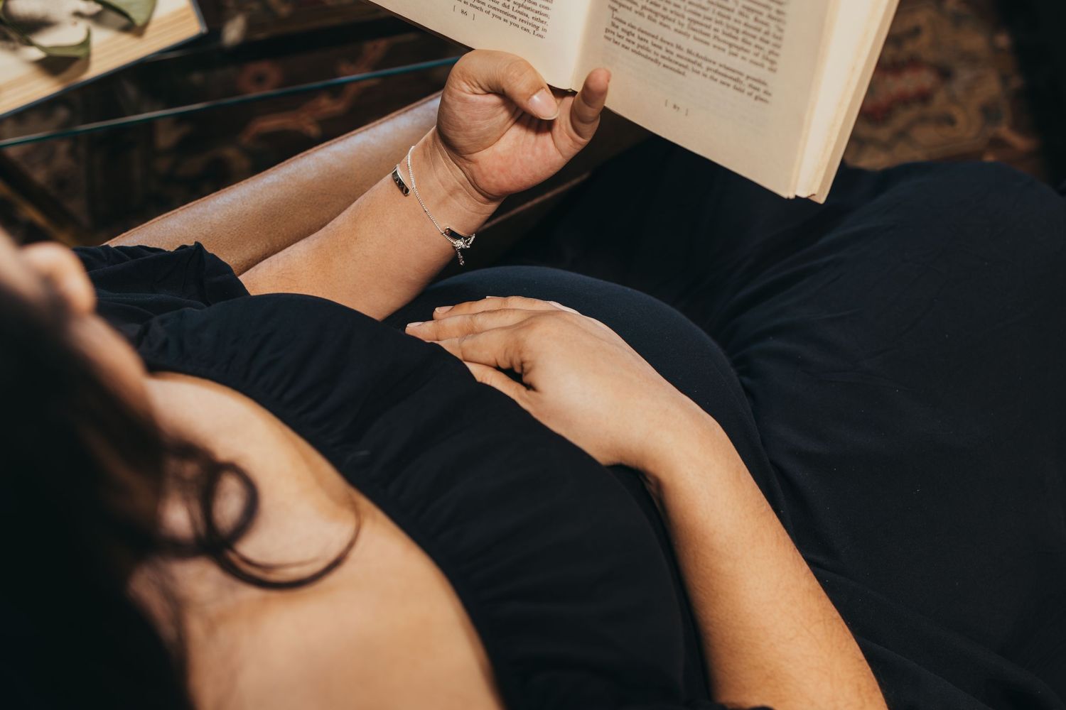 Close-up of pregnant belly while reading book in black dress.