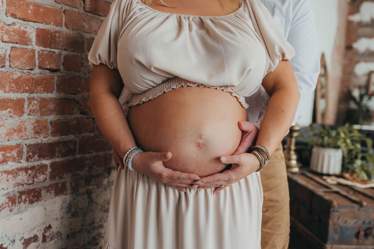Close-up shots of a pregnant person's belly in a cream-colored dress.