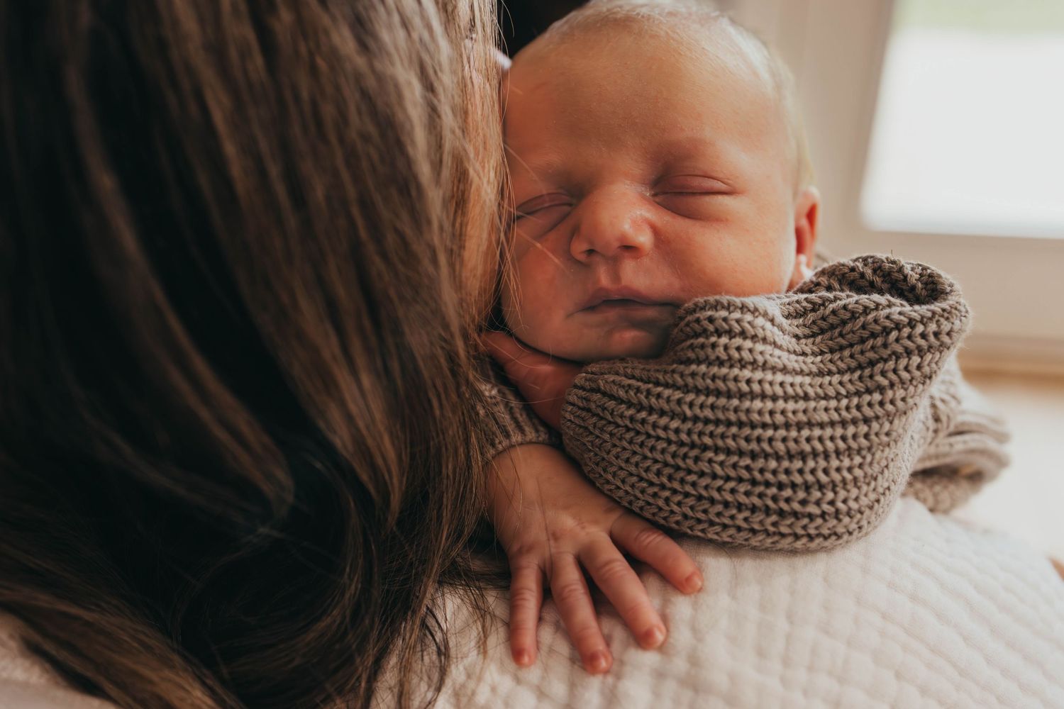 Baby resting peacefully on white bedding while being tenderly cradled.