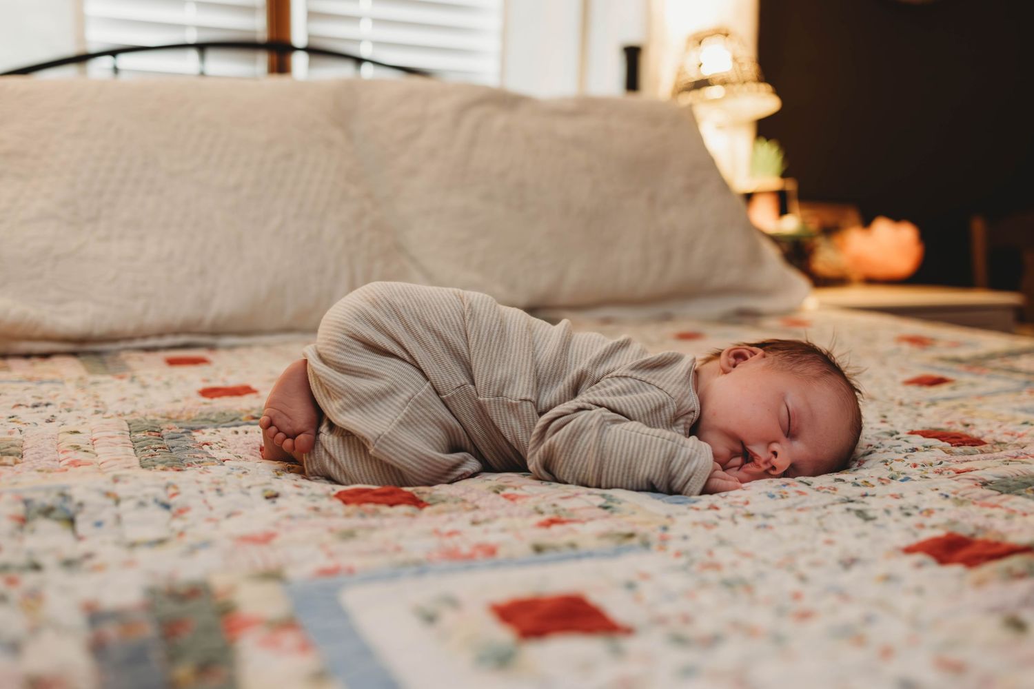 Baby resting on floral patterned blanket with soft lamp light in background.