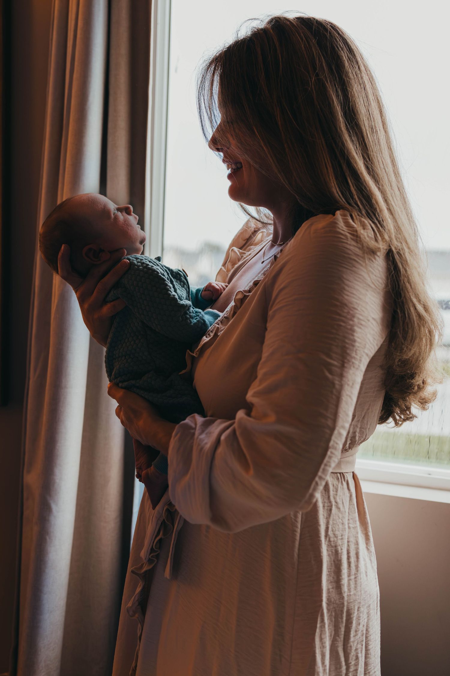 Silhouette by window showing tender moment with infant in natural light.