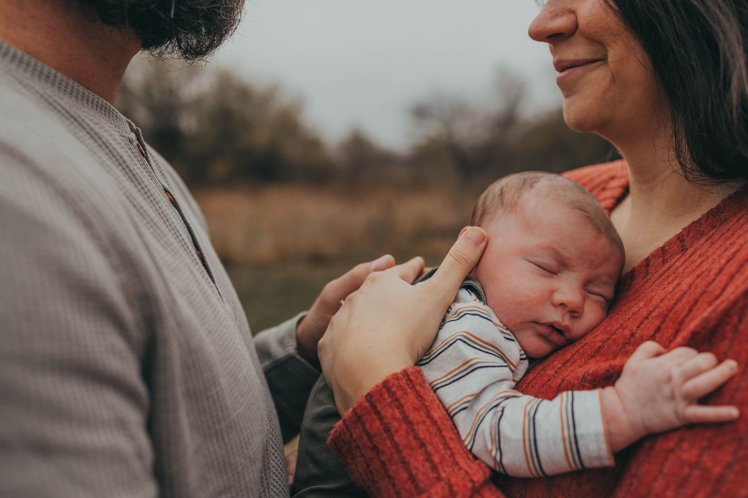 Tender family moment outdoors with red sweater and striped clothing.