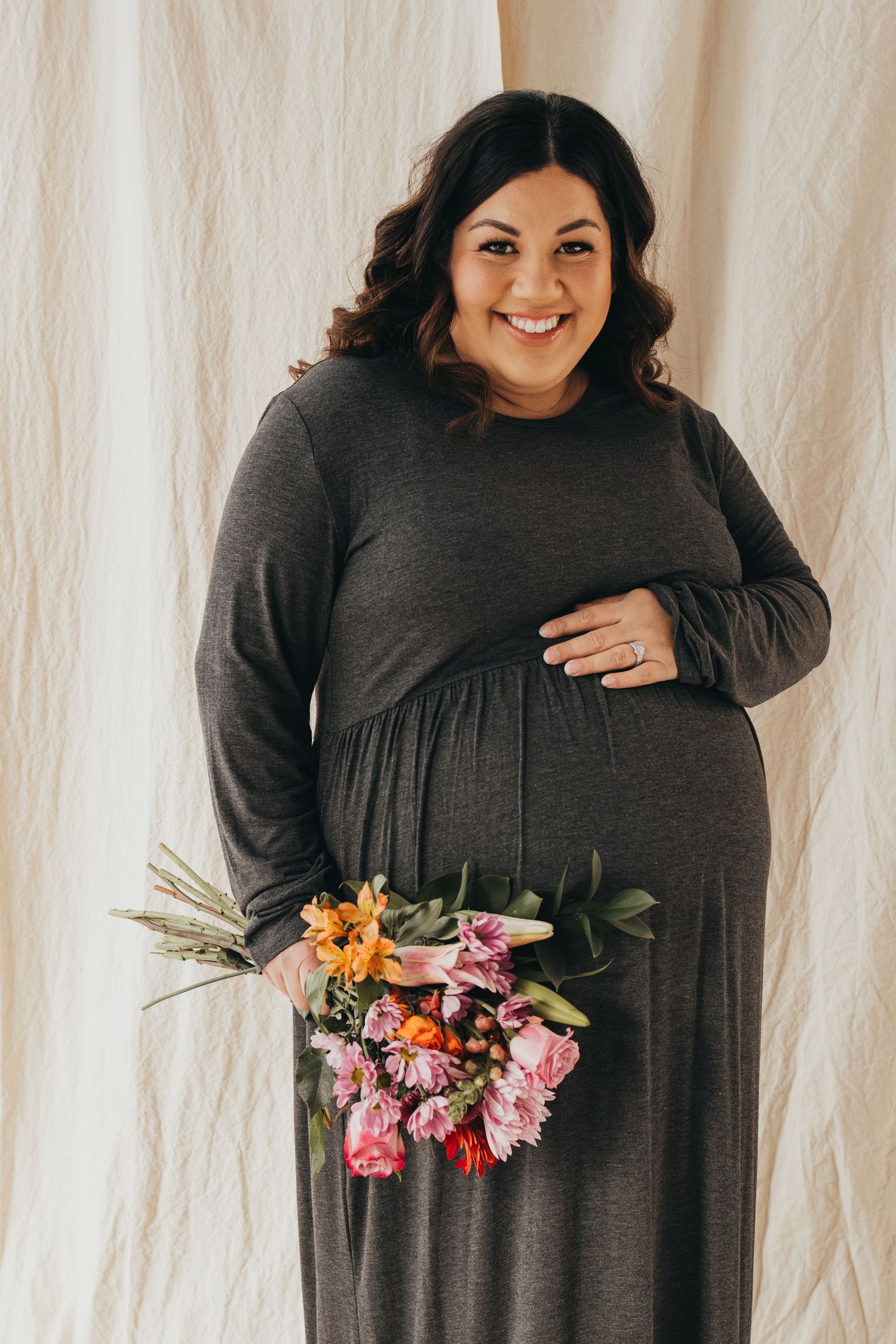 Maternity photo series with woman in gray dress holding colorful flowers.