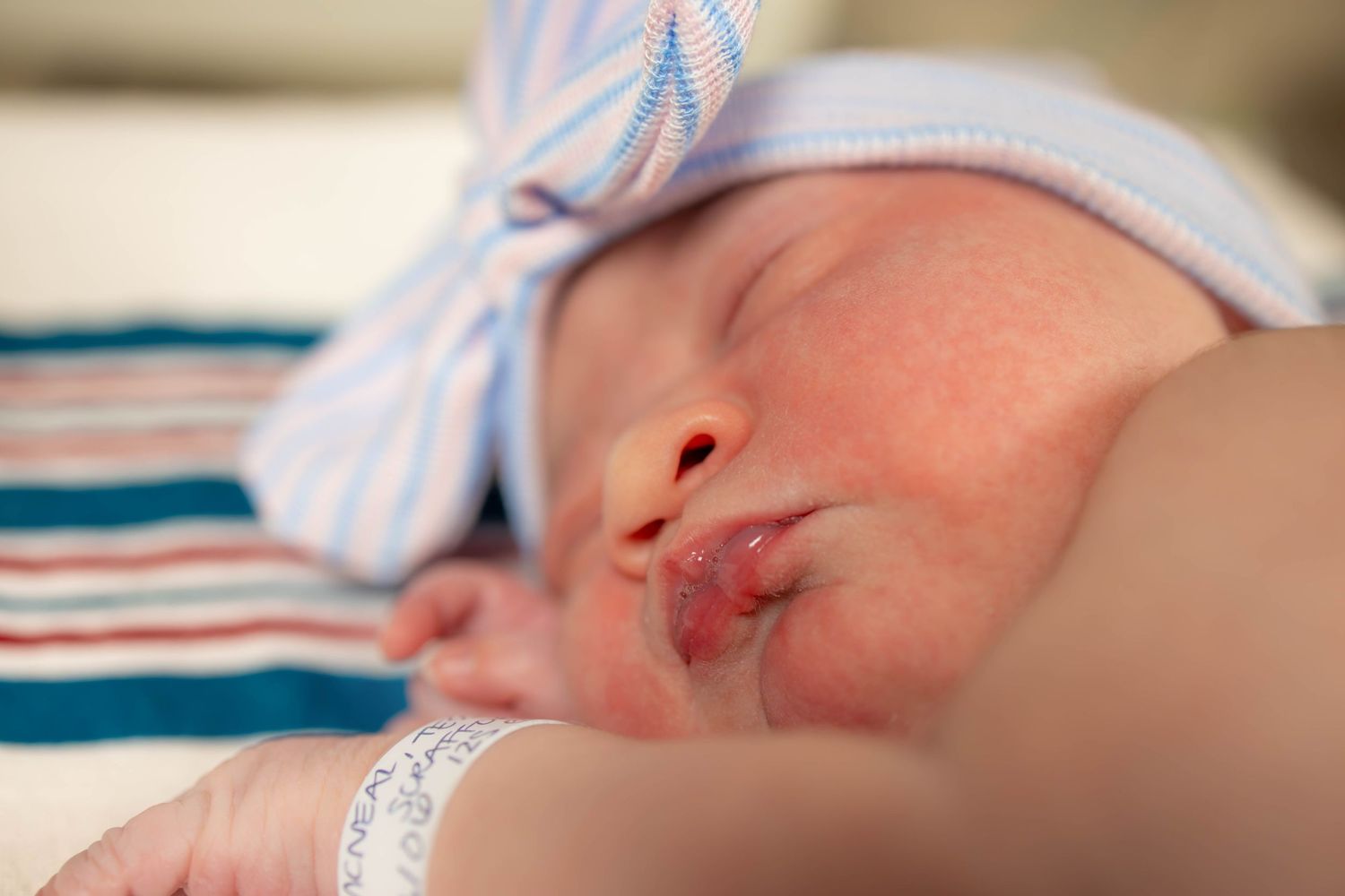 Close-up view of a peaceful newborn baby wearing a blue and white striped hospital cap.