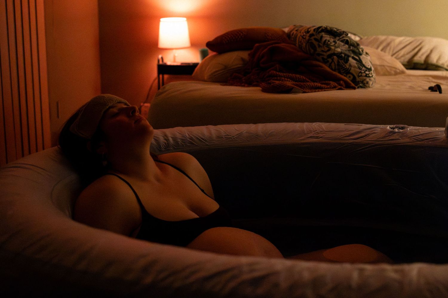 A dimly lit bedroom with warm orange lighting from a bedside lamp creating a cozy ambiance.