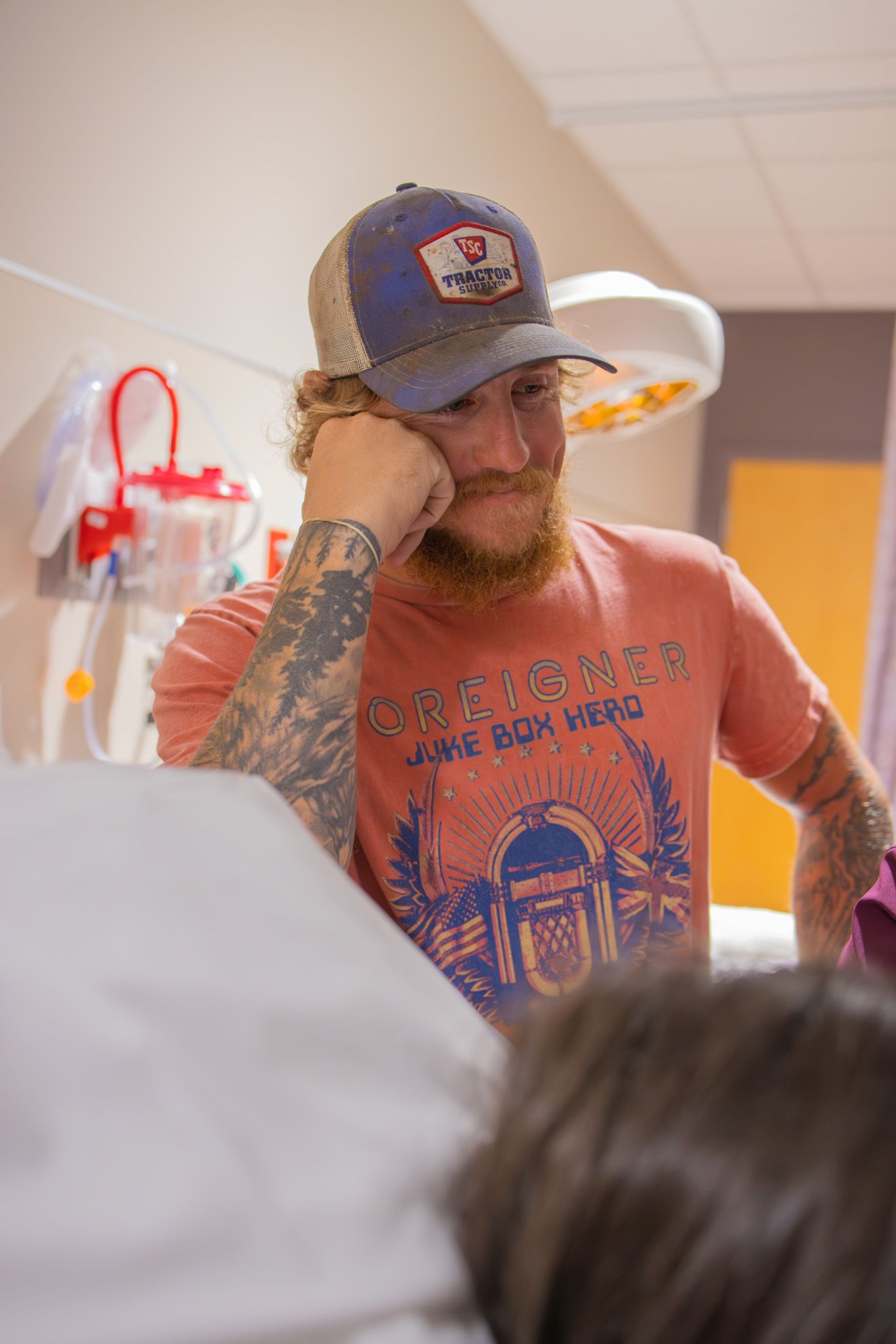 Person in a baseball cap and graphic t-shirt in a medical setting.