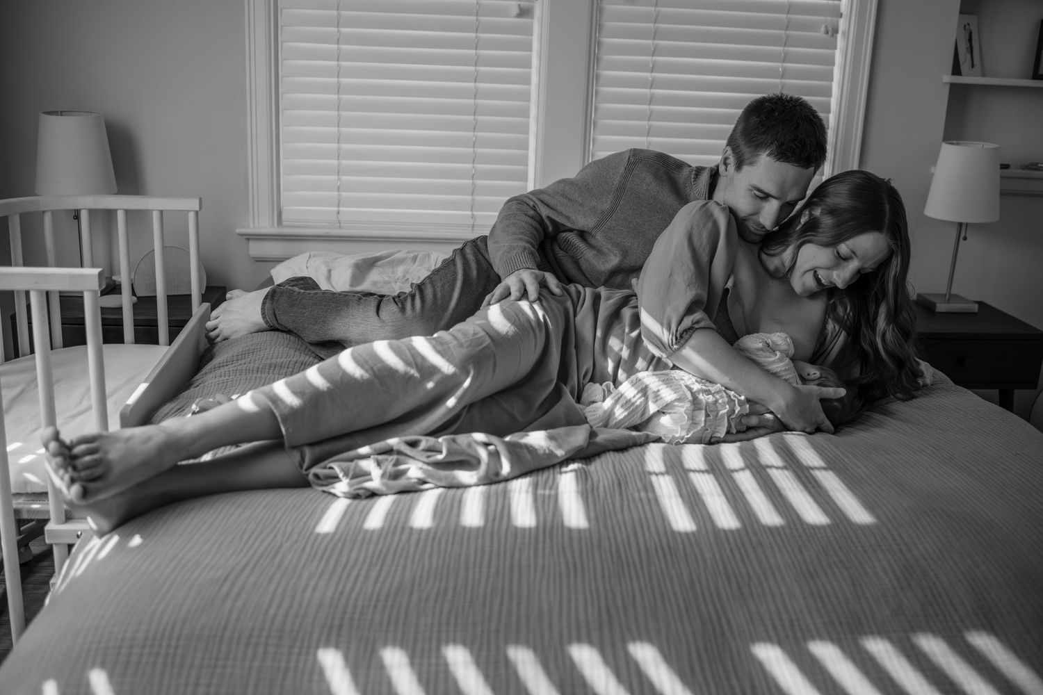 Family resting together on striped bedding in natural window light.