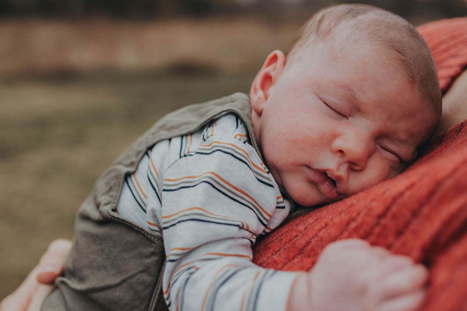 Sleeping infant in striped outfit resting against red knit sweater.