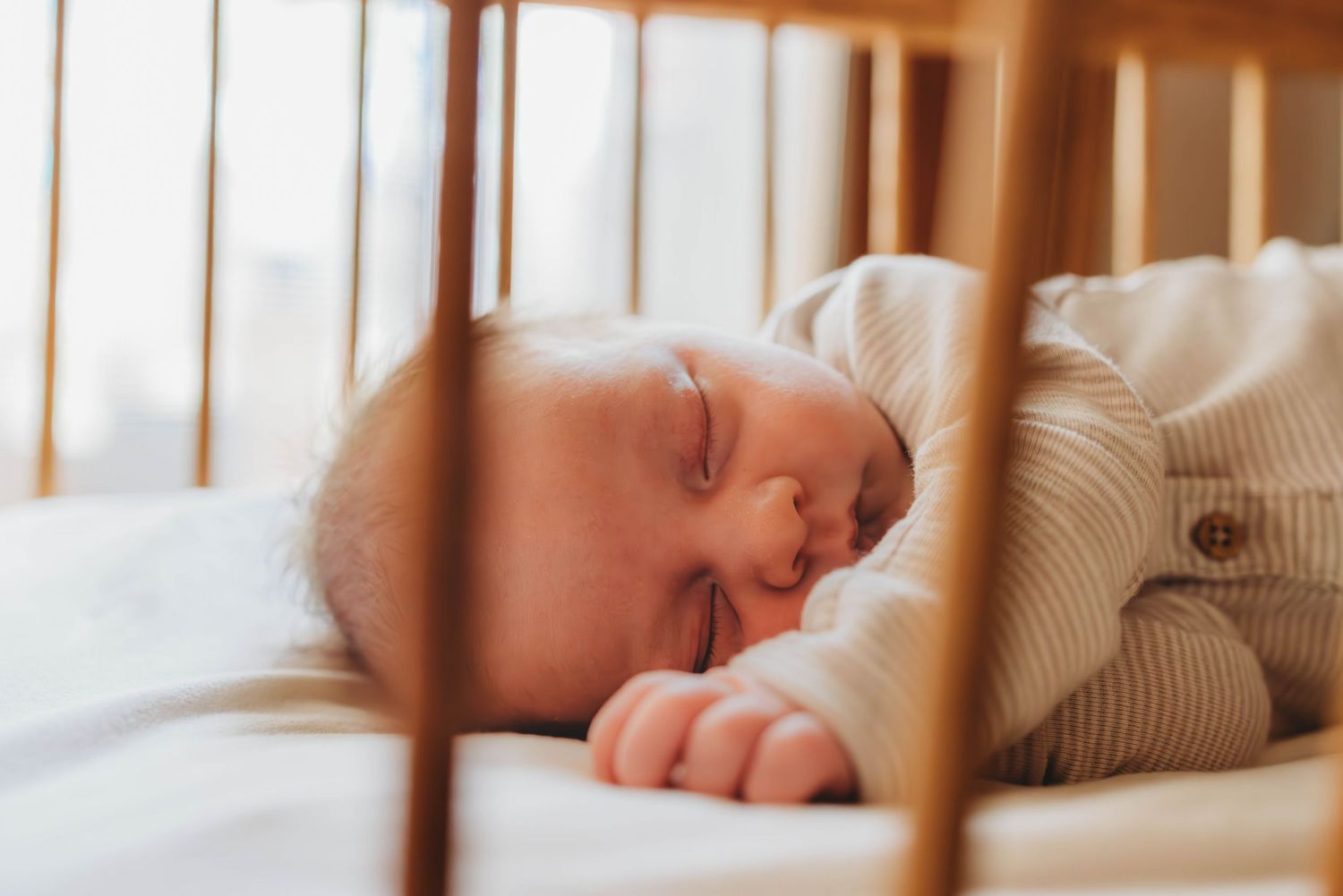 Baby napping peacefully in crib with sunlight streaming through window blinds.