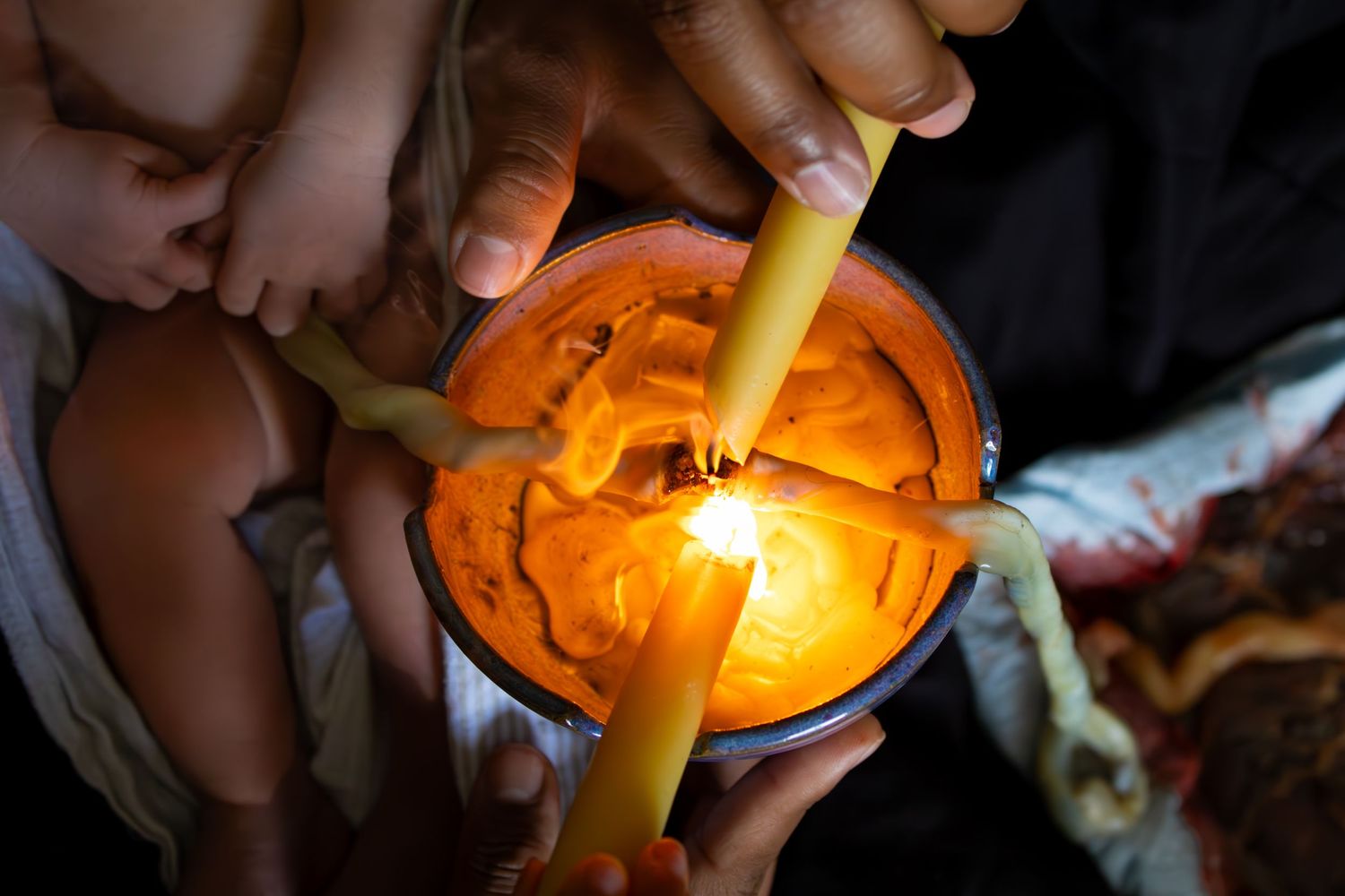 Person lighting orange candles in a dark setting creating a warm ambiance.