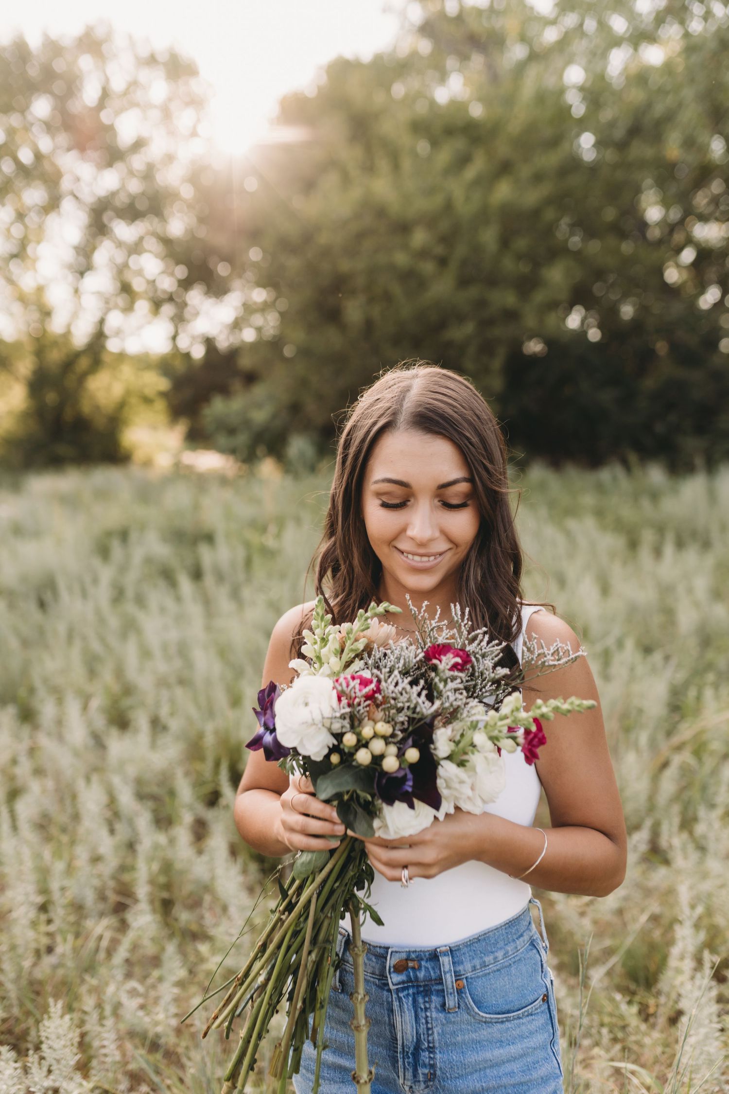 Person holding a colorful bouquet of fresh flowers in a sunny field of tall grass.