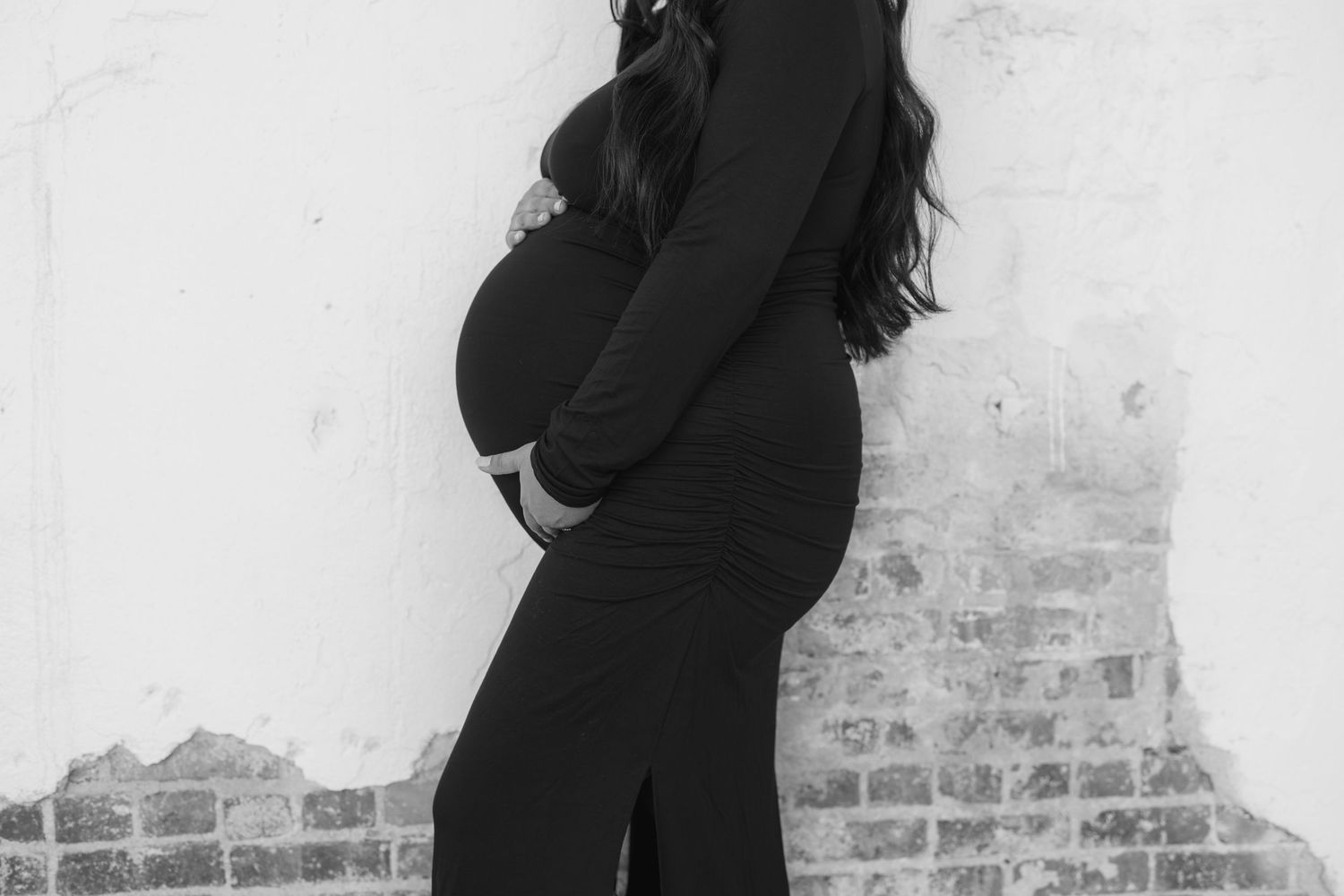 Black and white maternity photos against textured brick wall.