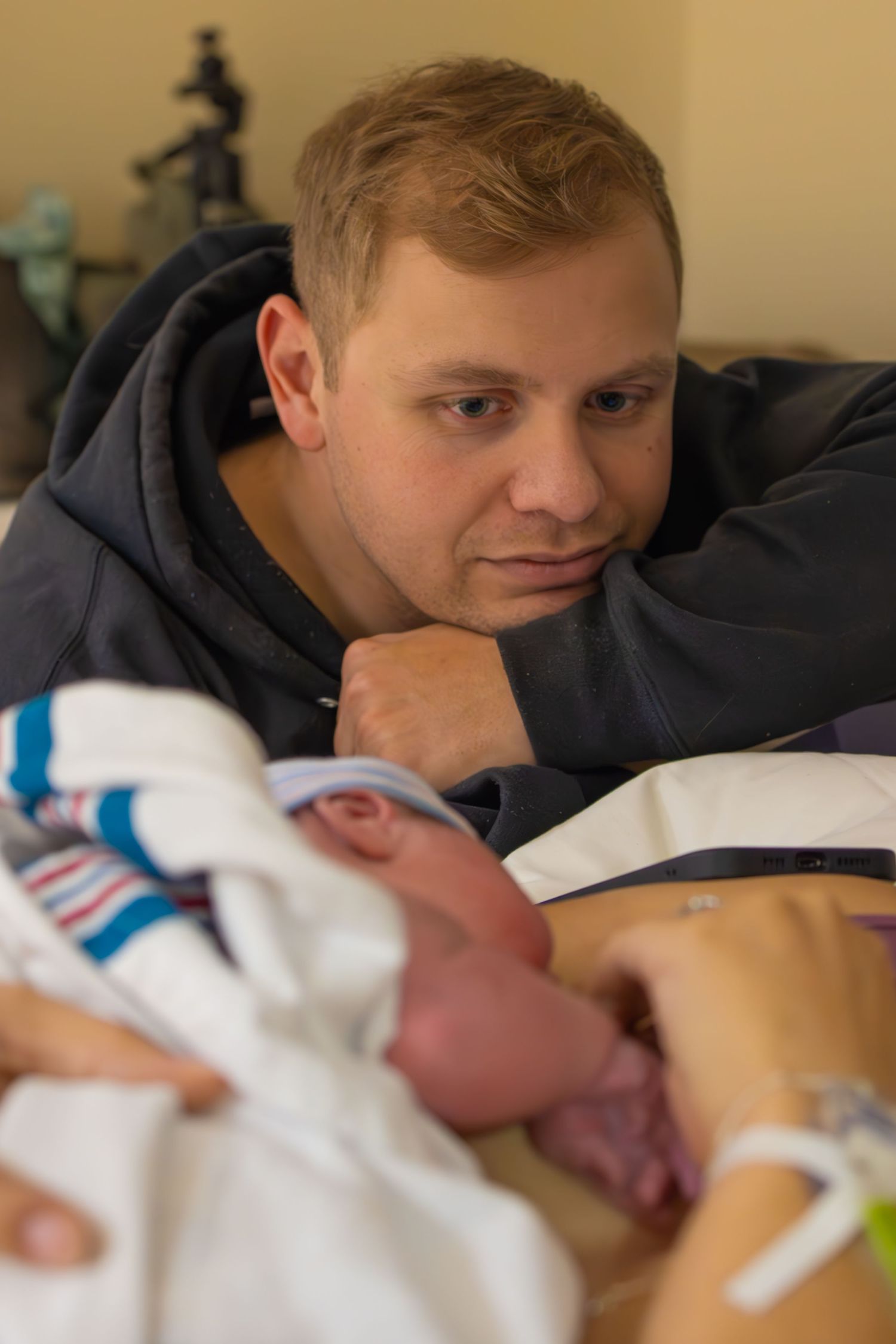 A newborn baby rests in a hospital bassinet while being watched over with a loving gaze.