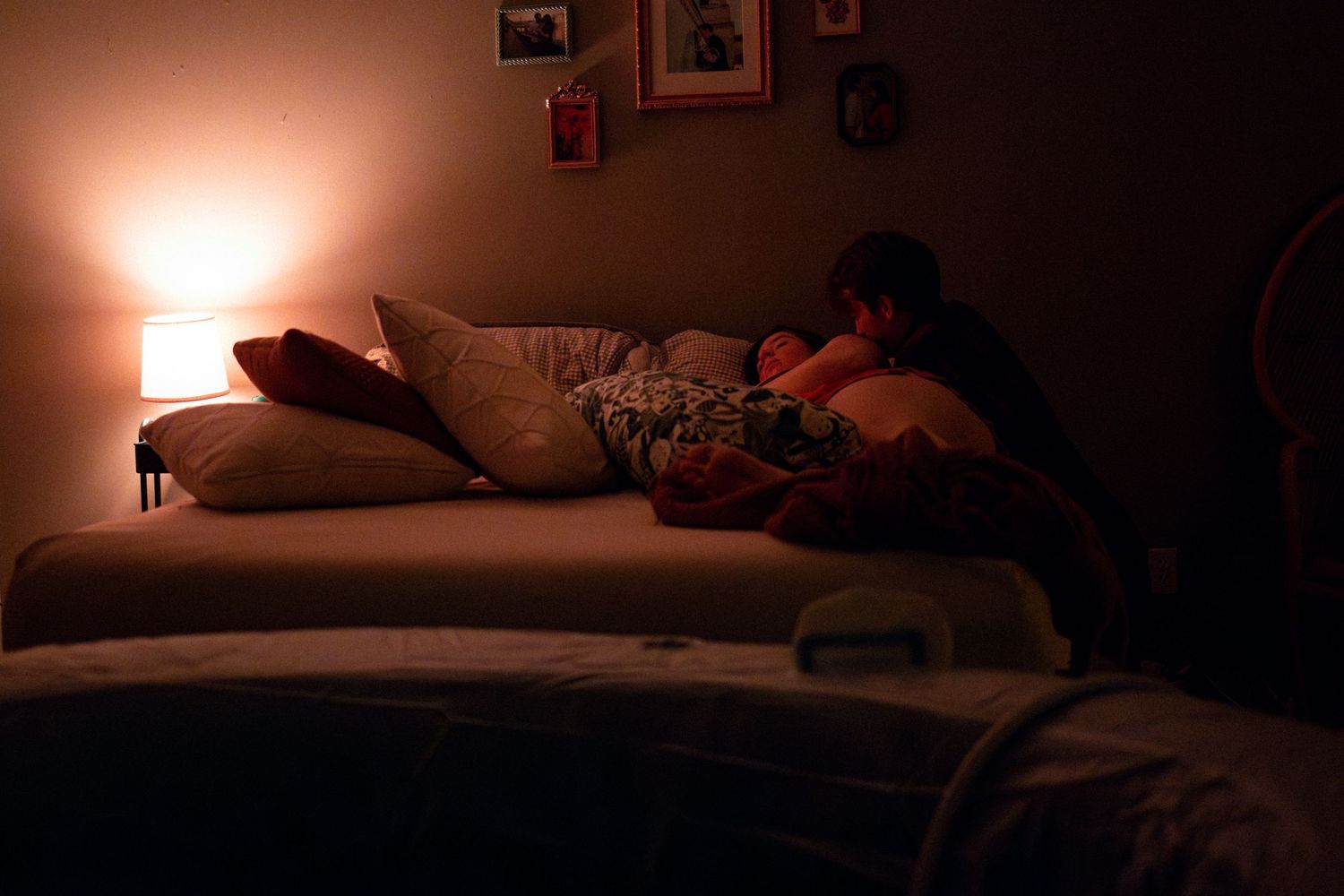 A dimly lit room shows a cozy bed with rumpled sheets and pillows in warm, ambient lighting.