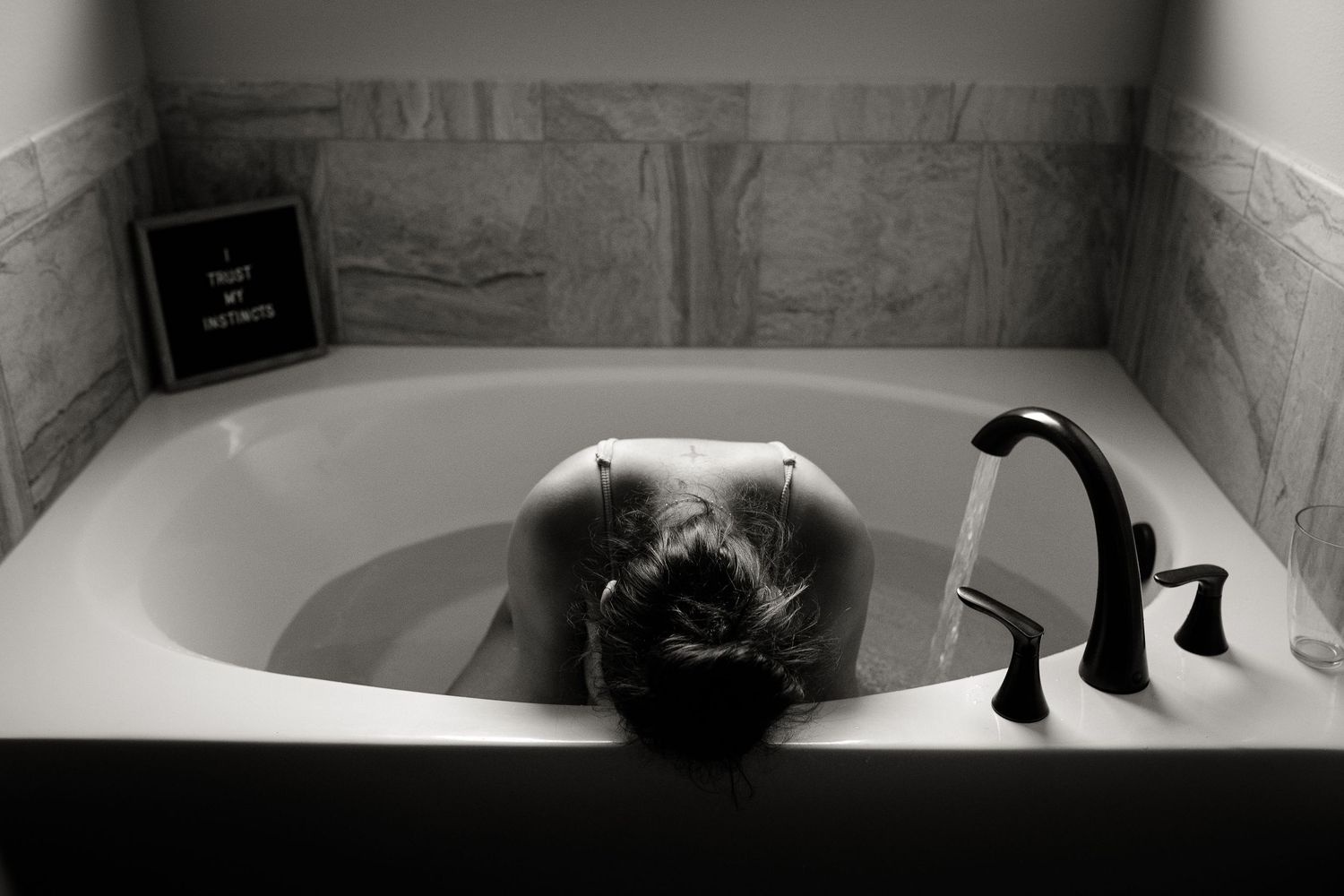 A pregnant woman relaxes in a bathtub during a maternity photoshoot in black and white.