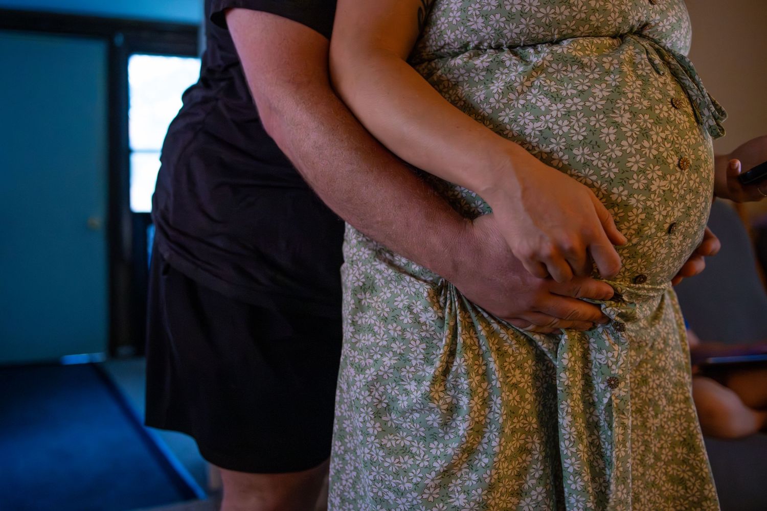 Hands gently rest on a pregnant belly covered in a floral patterned dress.