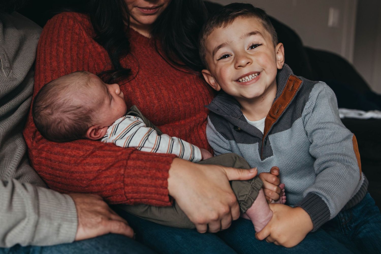 Family cuddling together on couch wearing casual clothes in warm indoor lighting.