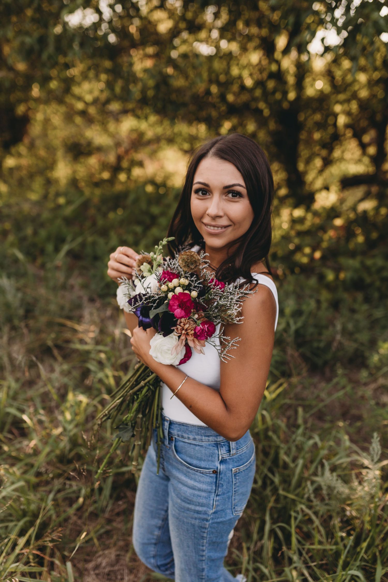 Woman in casual attire holding a colorful bouquet of wildflowers outdoors.