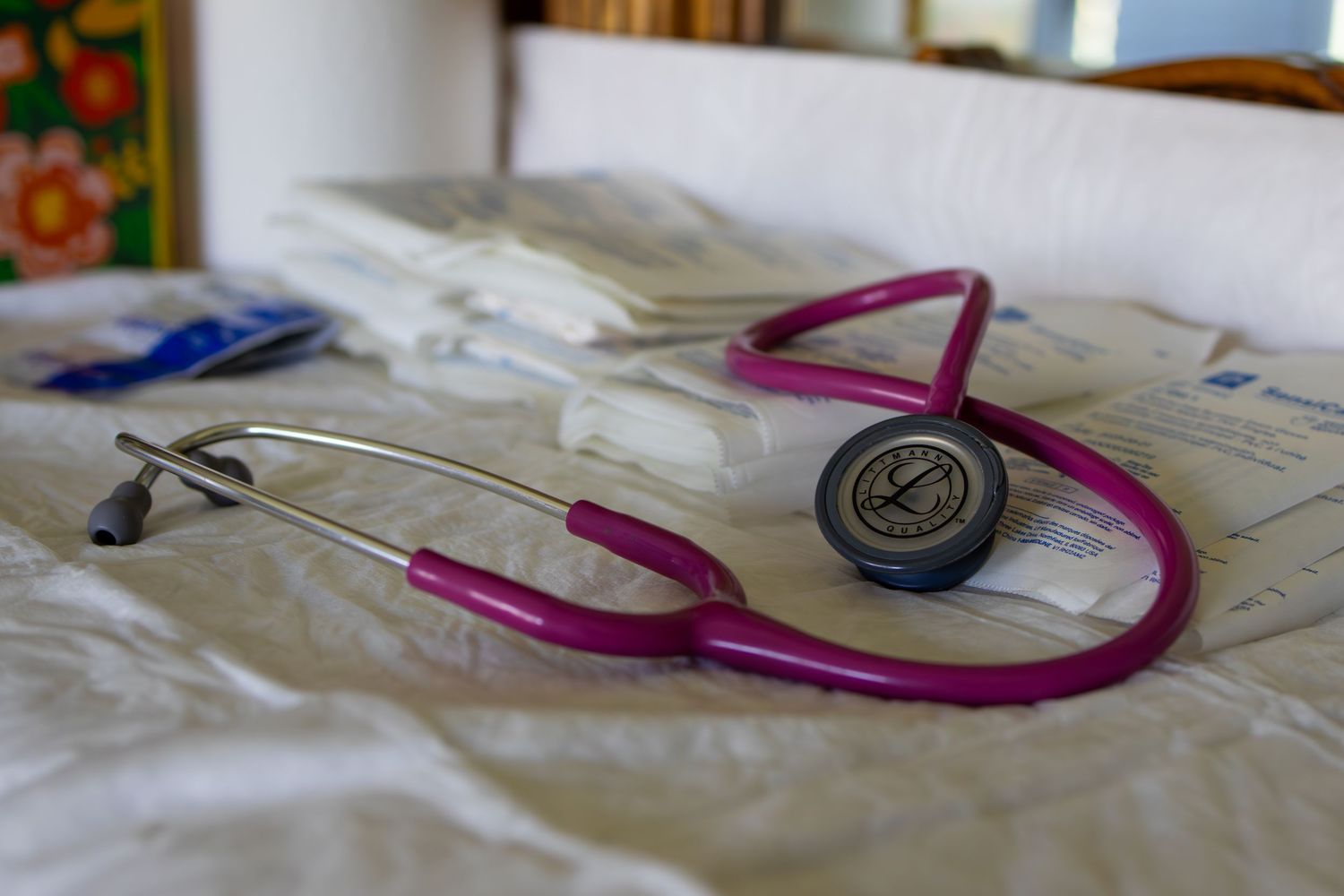 Pink stethoscope lying on white medical examination table with other medical tools.