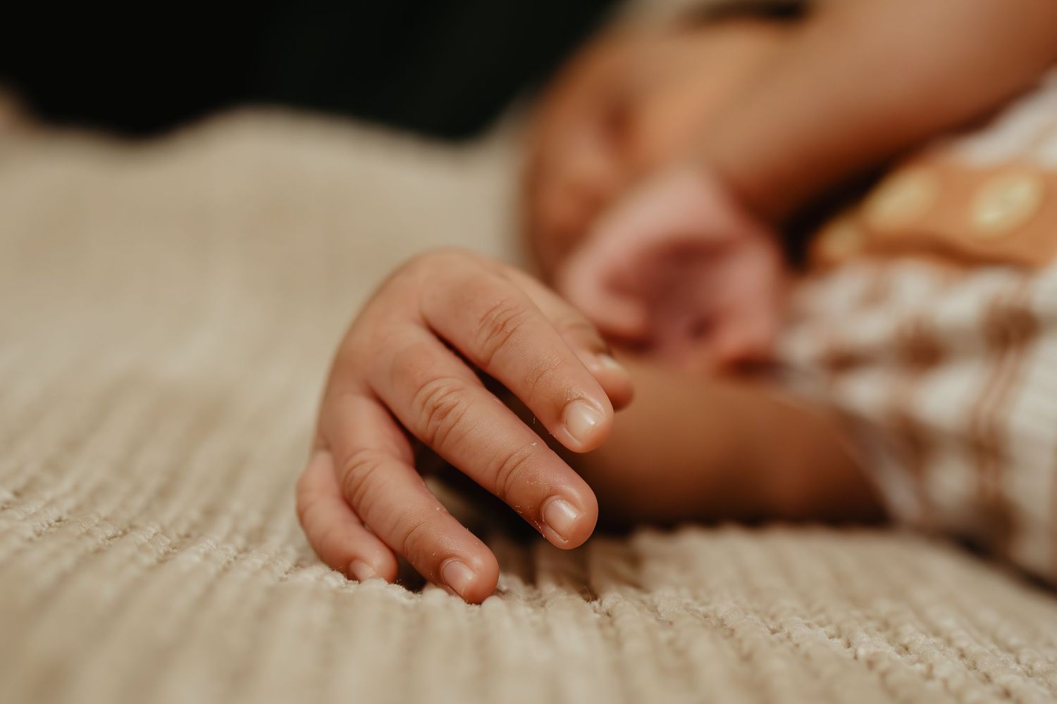 Small infant hand resting on textured beige fabric.