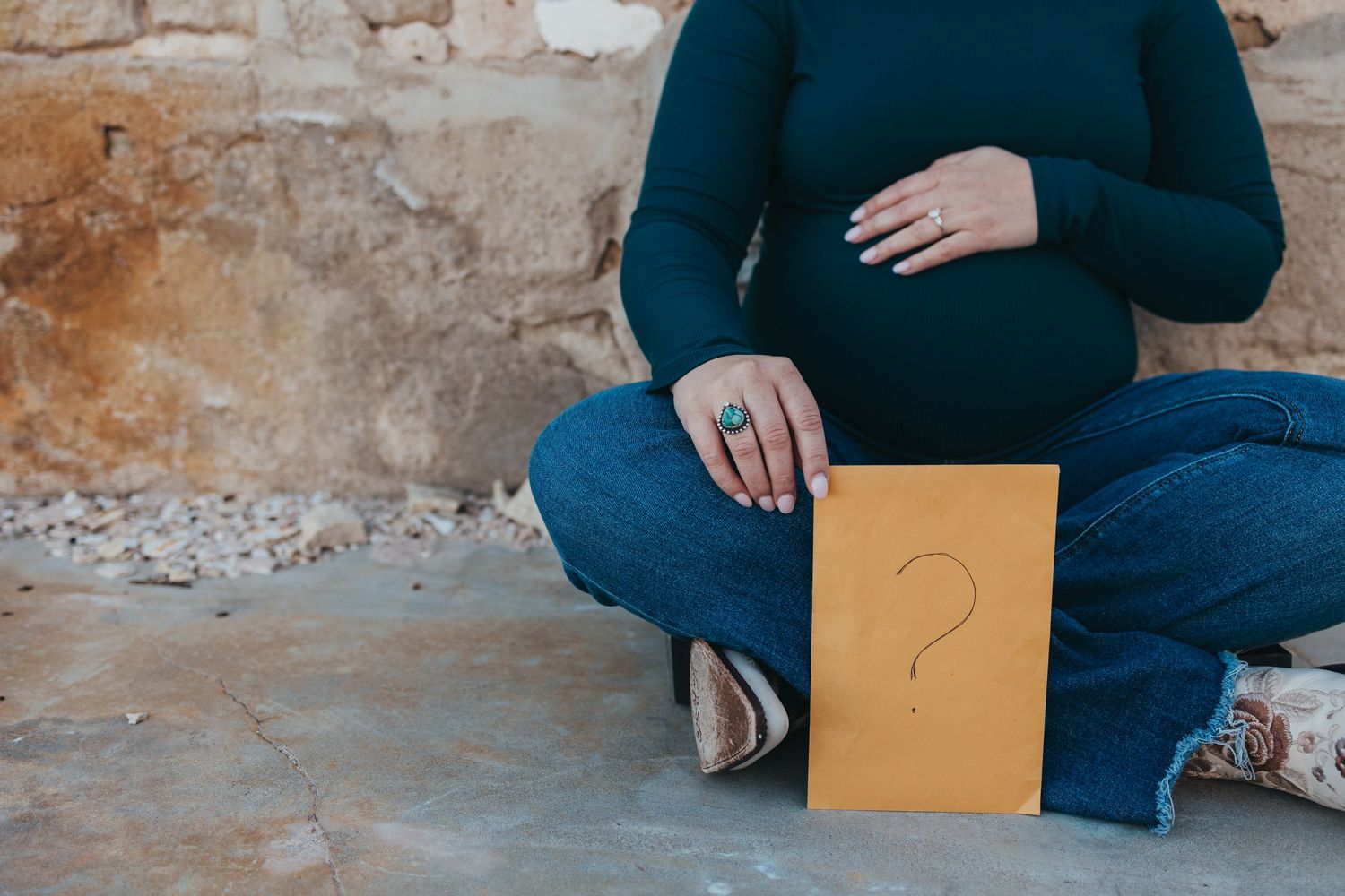A person in a blue sweater holds a brown envelope while sitting on a rustic stone ledge.