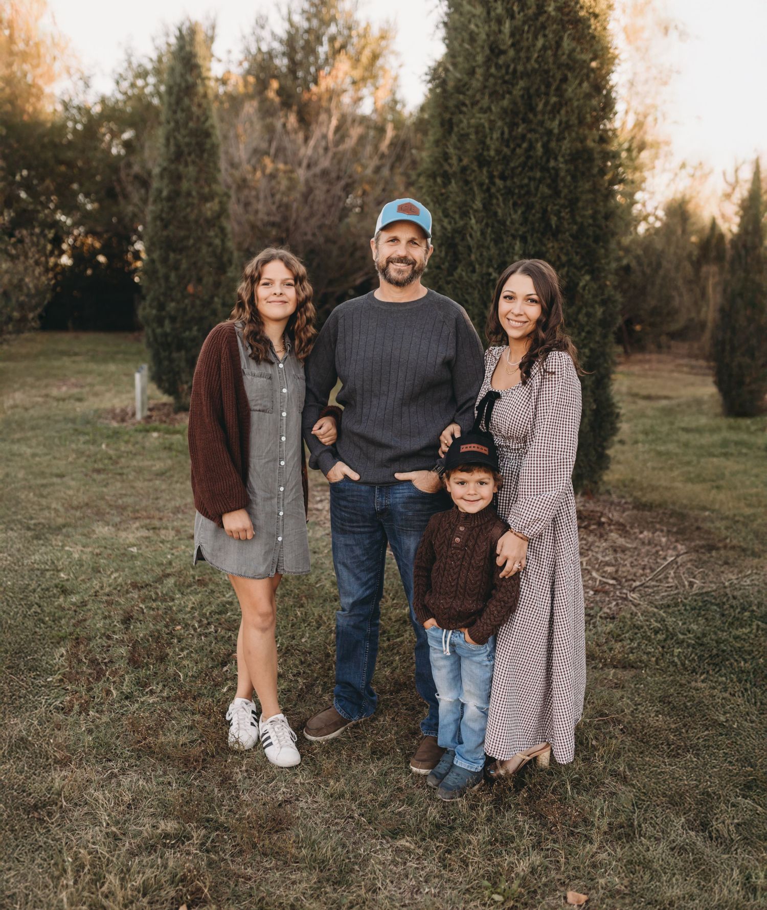 Family group photo in casual attire against evergreen trees at dusk.