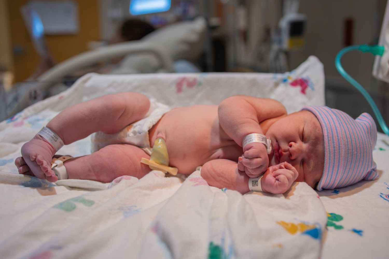 Newborn baby lying in a hospital bassinet with medical monitoring equipment.