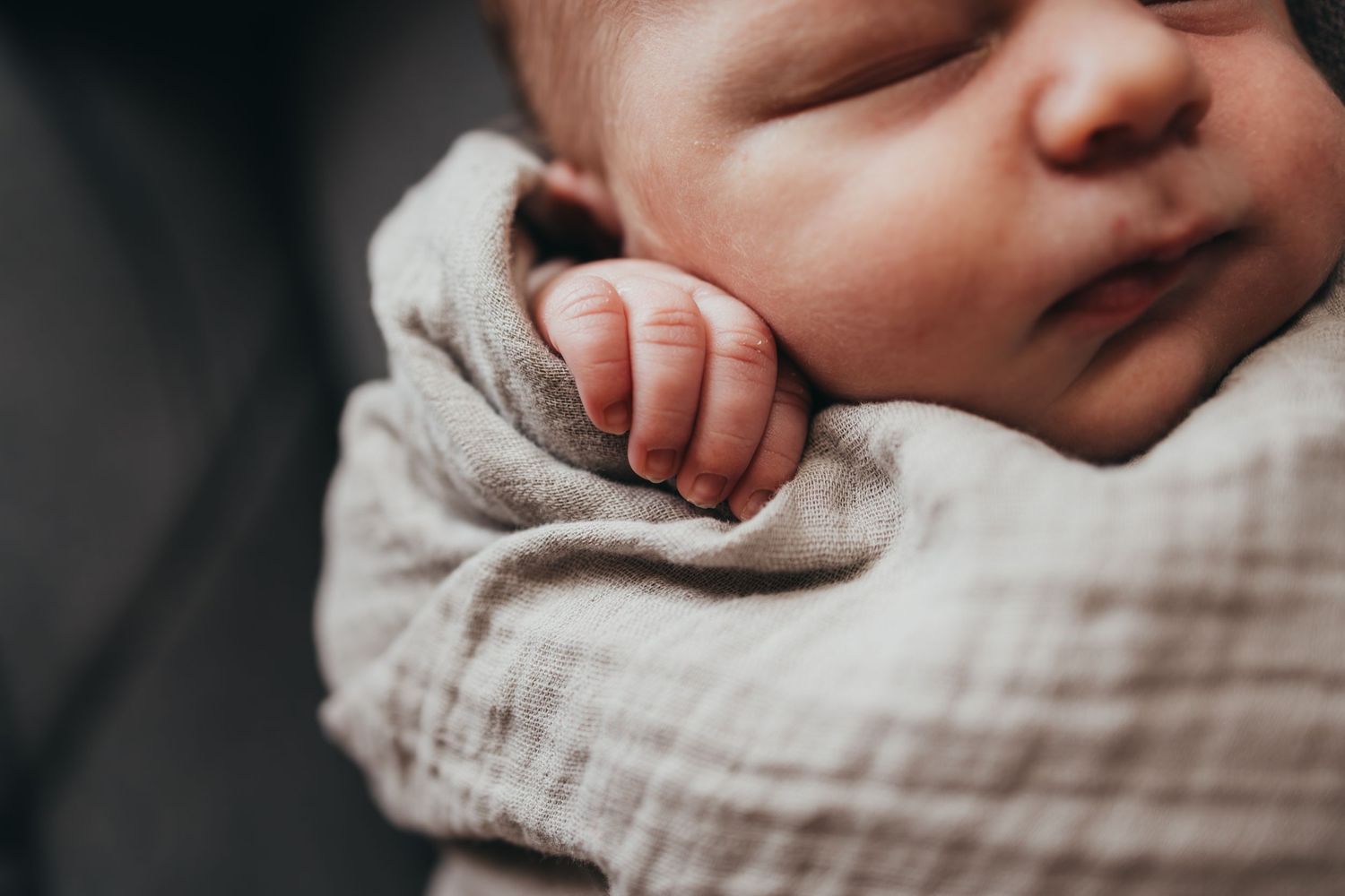 Close-up black and white photograph of a sleeping newborn baby wrapped in a light-colored blanket.
