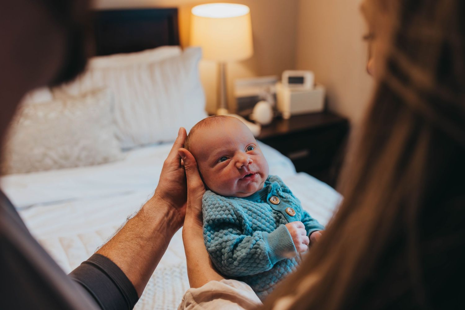 Intimate nursery moment with baby in blue outfit on white bedding.