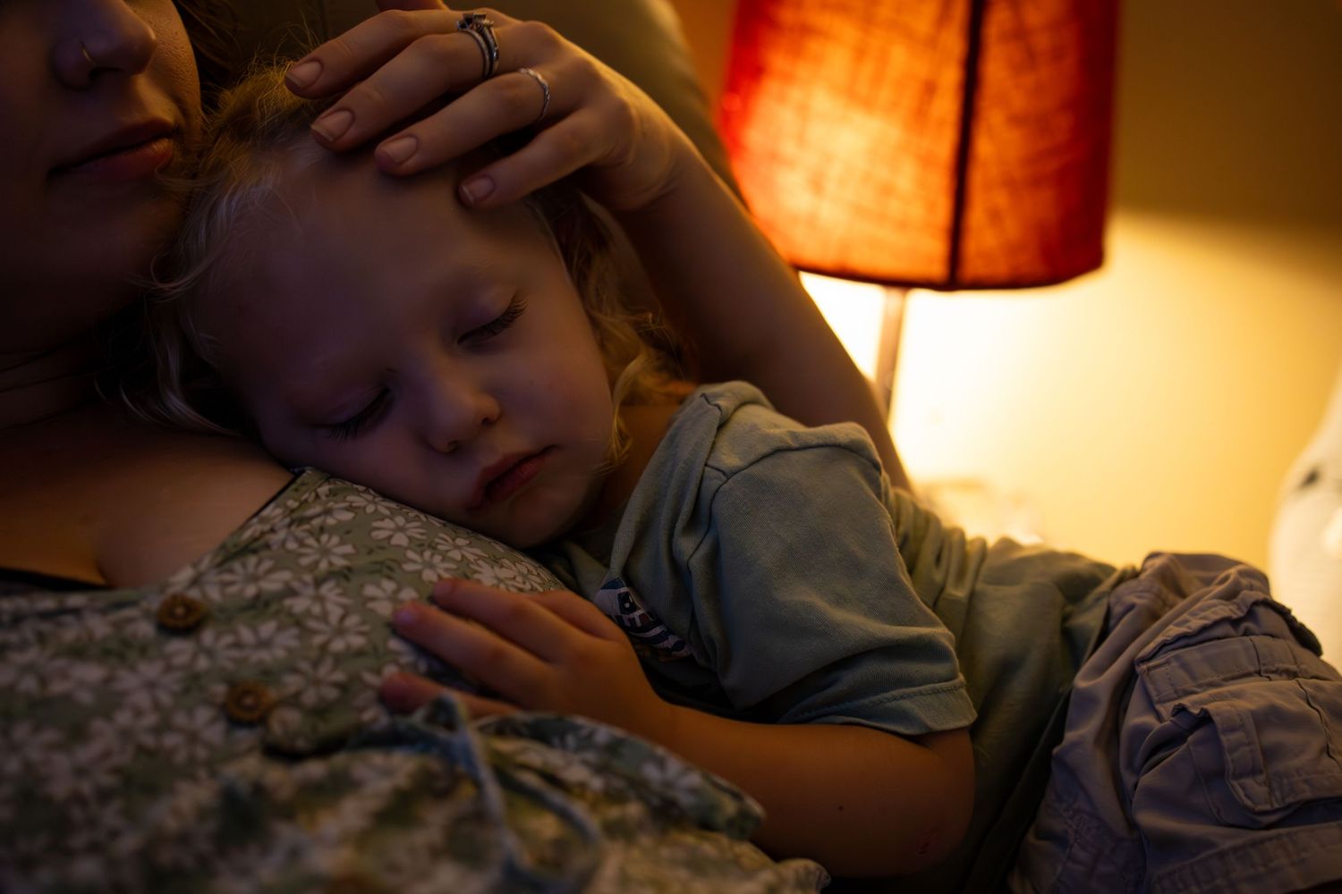A small child sleeps peacefully against a floral dress in warm lamp light.