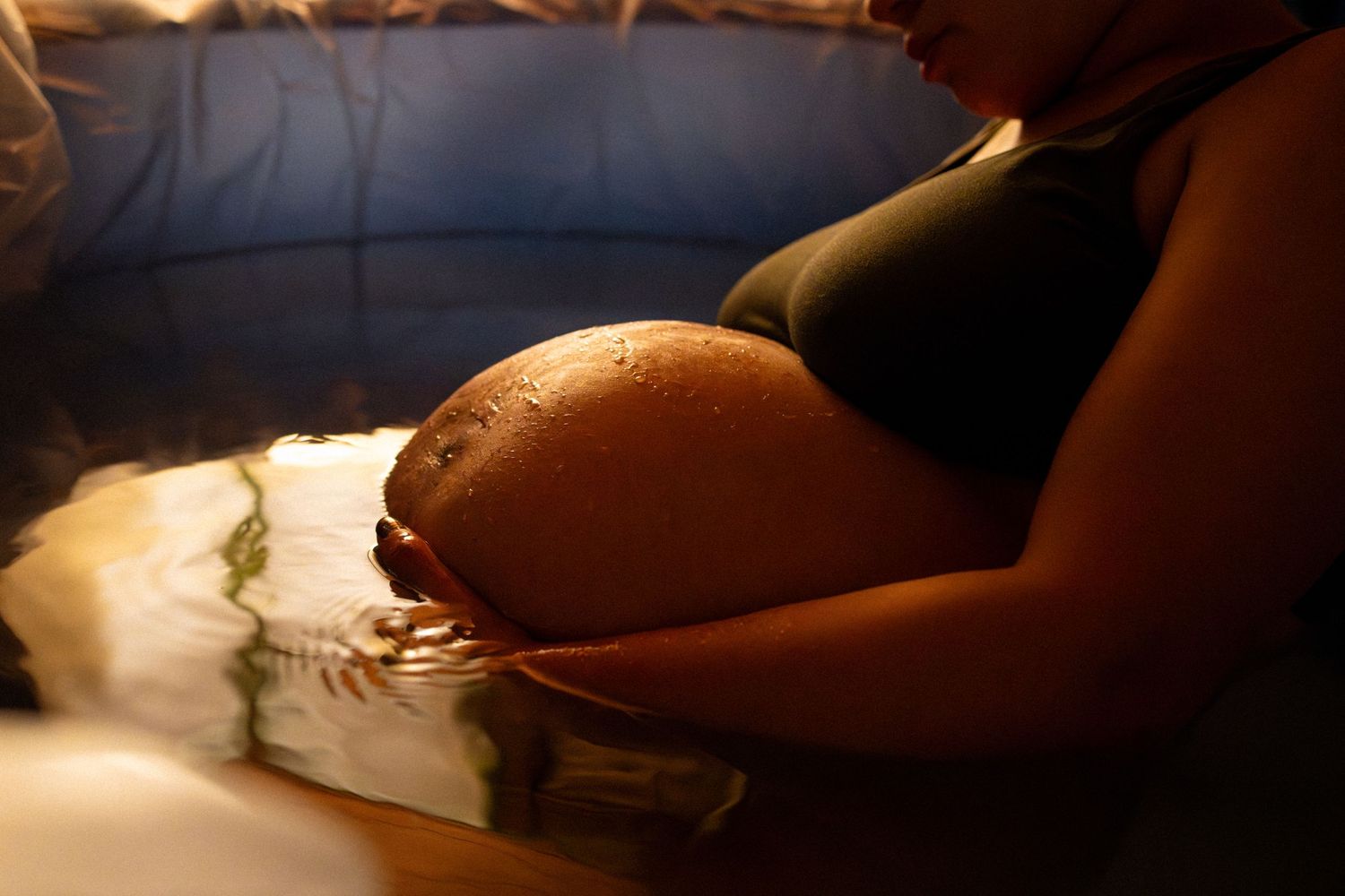 Pregnant woman relaxing in a warm water birth pool, cradling her belly during labor.