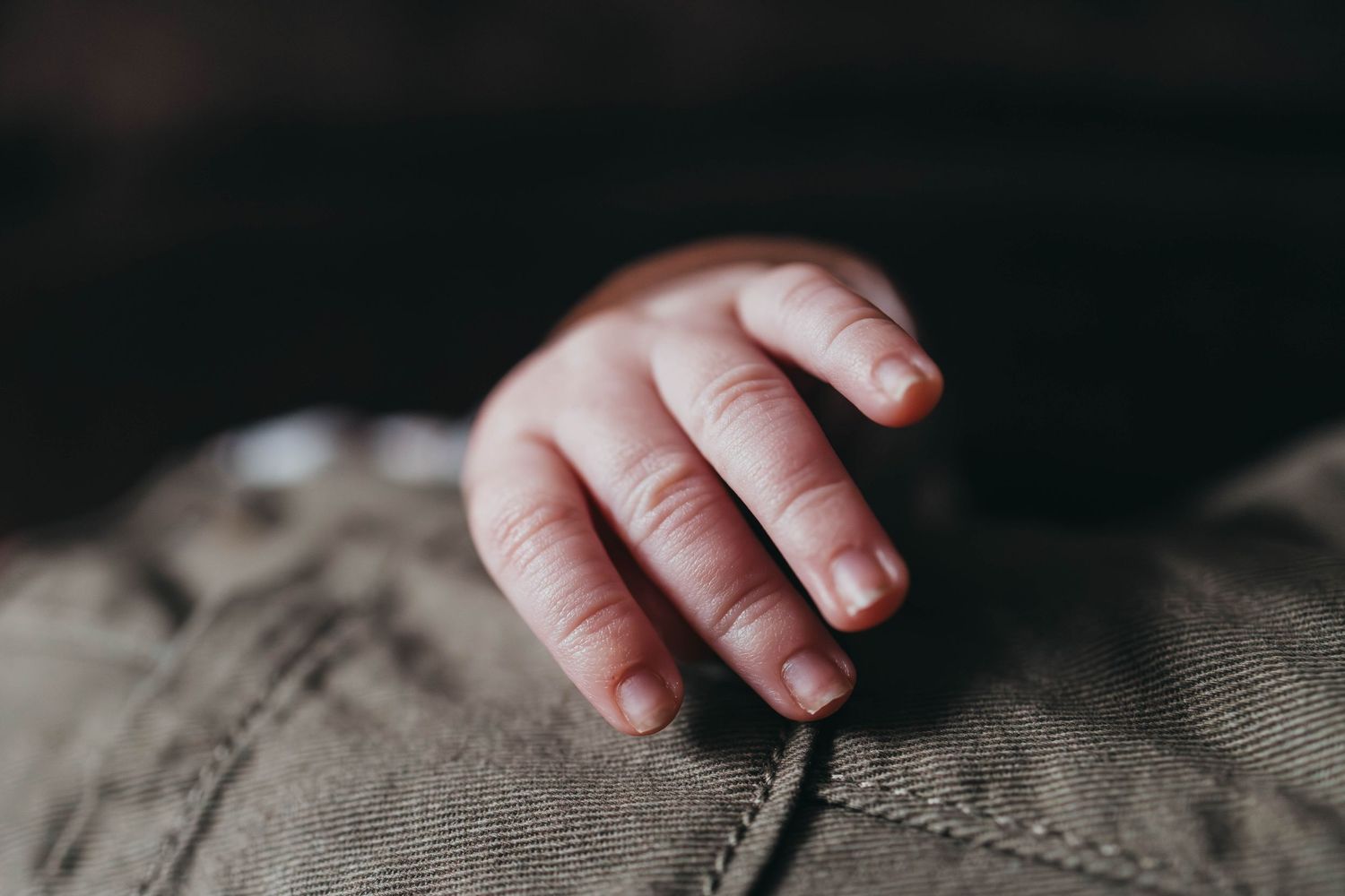 Small baby hand reaching out against textured gray fabric.