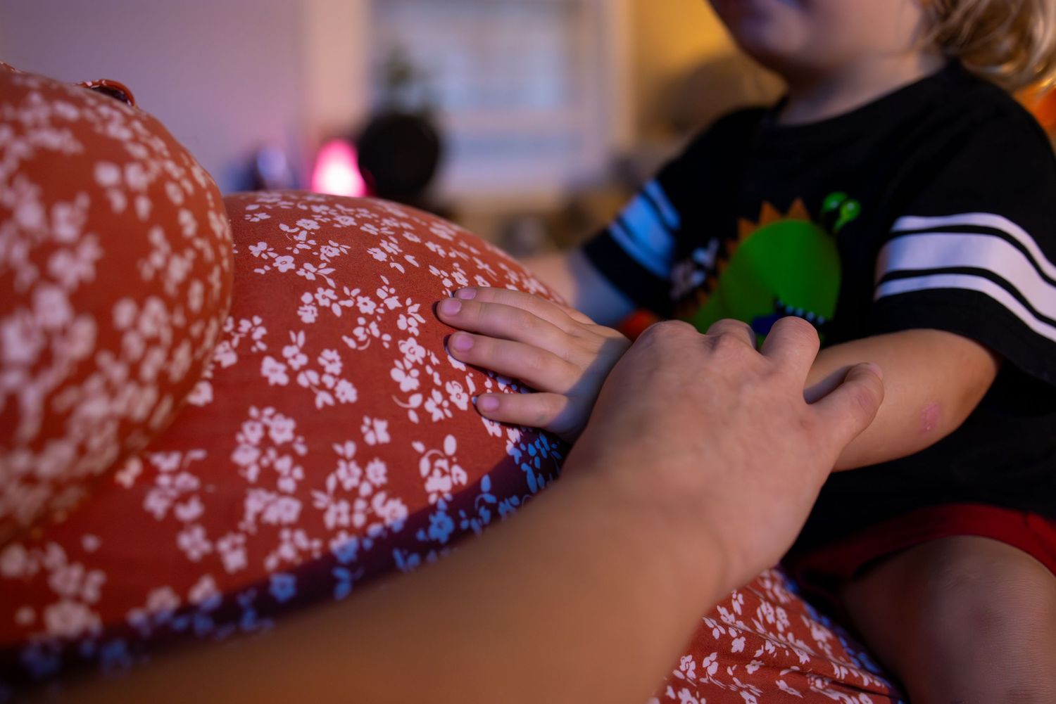 Hands rest on a red floral patterned fabric while interacting with a child.