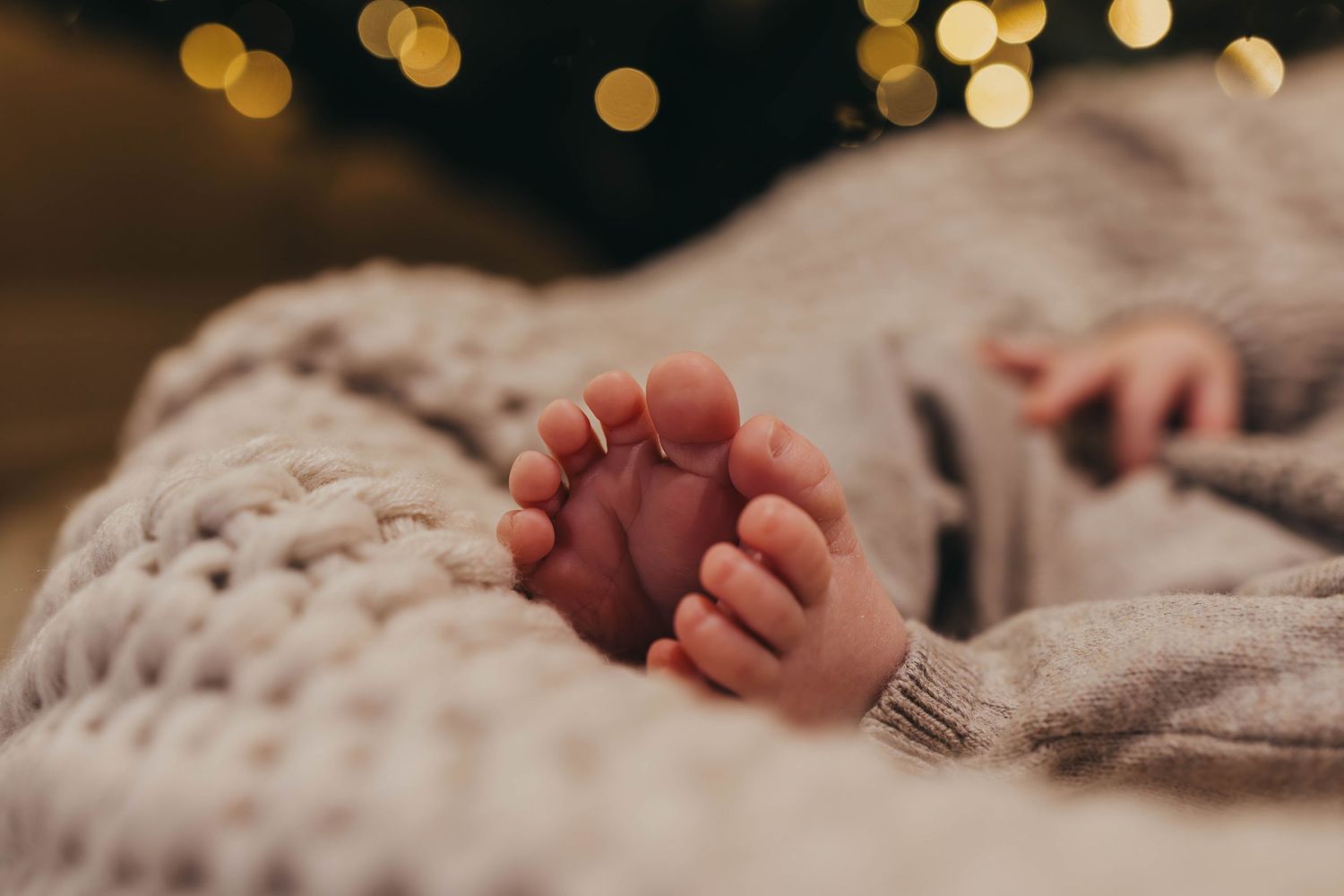 Baby feet detail shot with bokeh lights and textured blanket in background.