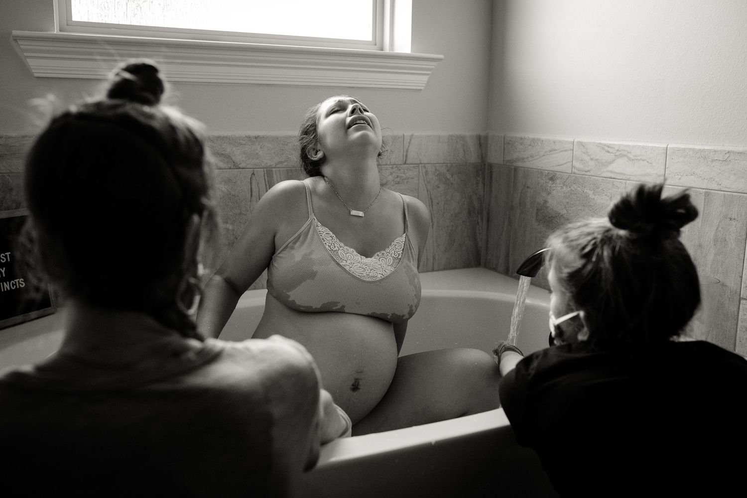 Natural light streams through window as expectant mother rests in tub.